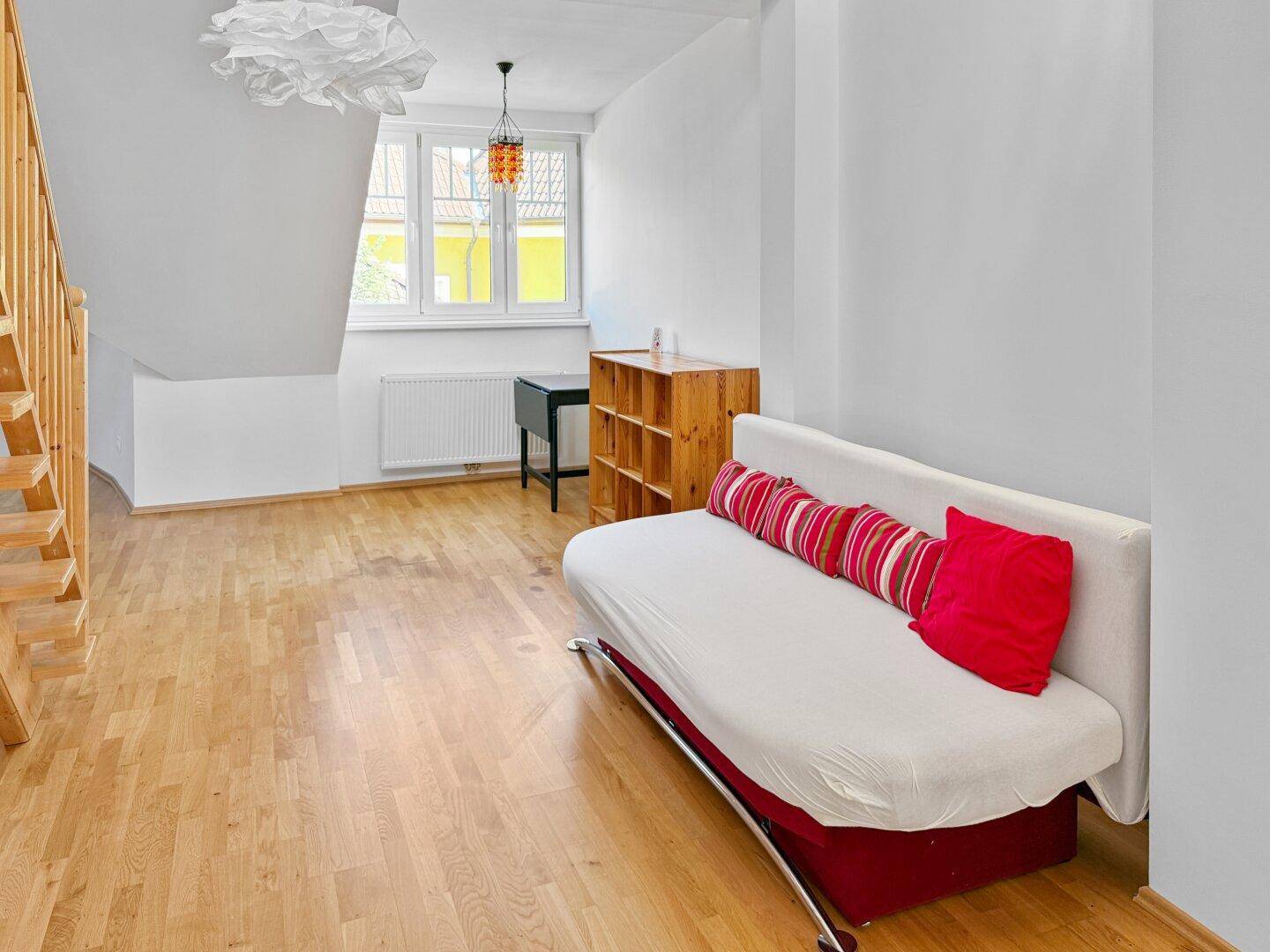 Offener Wohnbereich mit Holzboden, Sofa und Holztreppe zum oberen Geschoss.