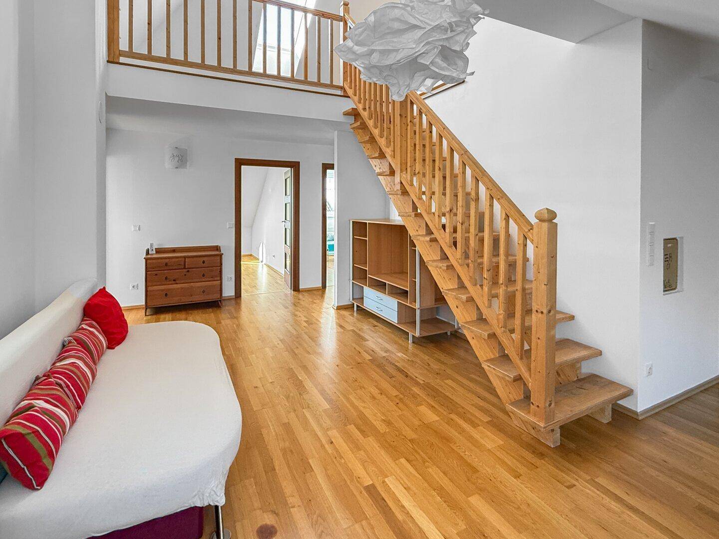 Geräumiger Wohnbereich mit Holztreppe, Sofa und Blick auf die Galerie.