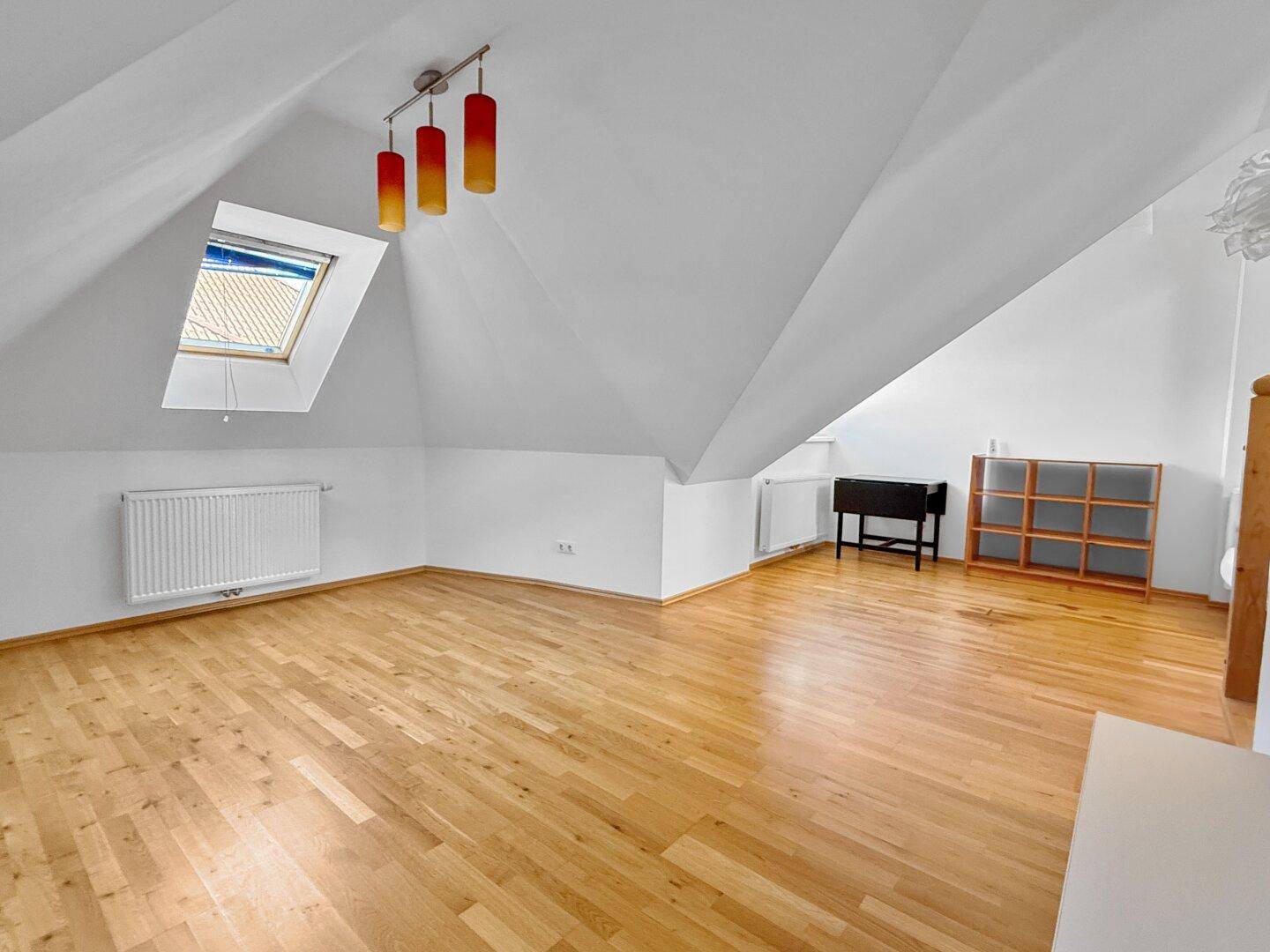 Heller Dachgeschossraum mit Holzboden, Dachfenster und moderner Beleuchtung.