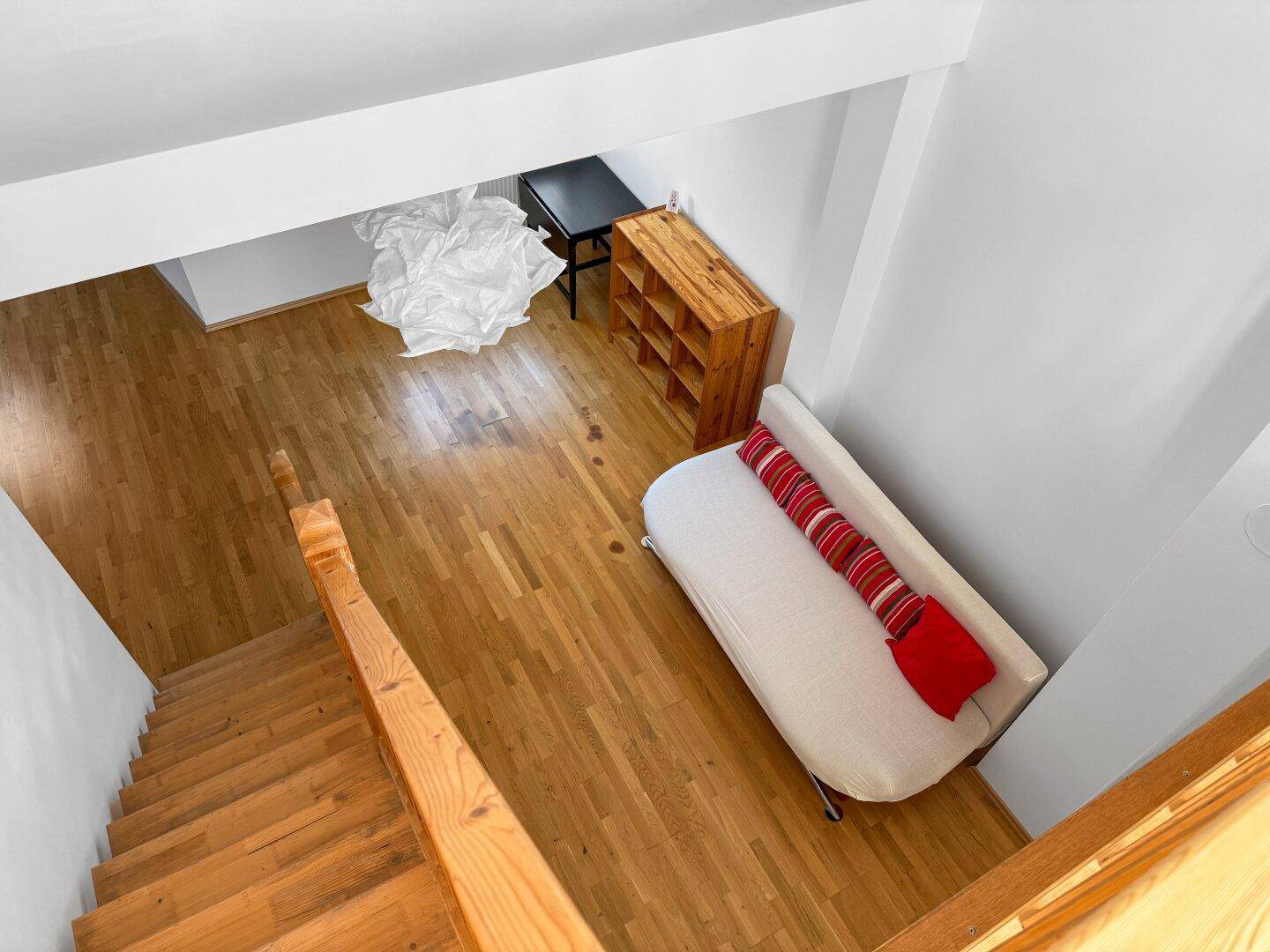 Blick von oben auf den offenen Wohnbereich mit Sofa und Holztreppe.