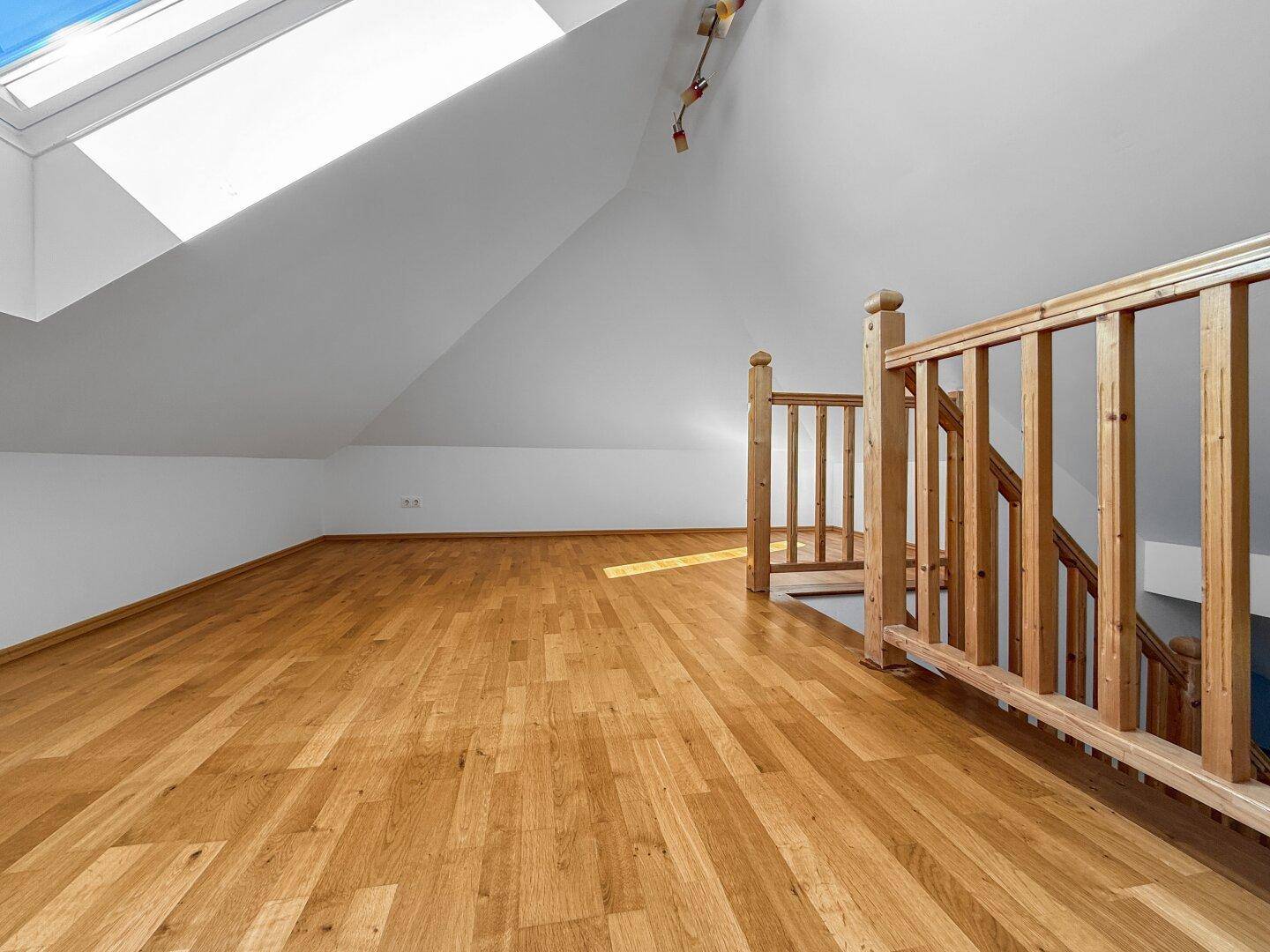 Geräumiger Dachgeschossraum mit Holzboden, Dachfenster und Holzgeländer.