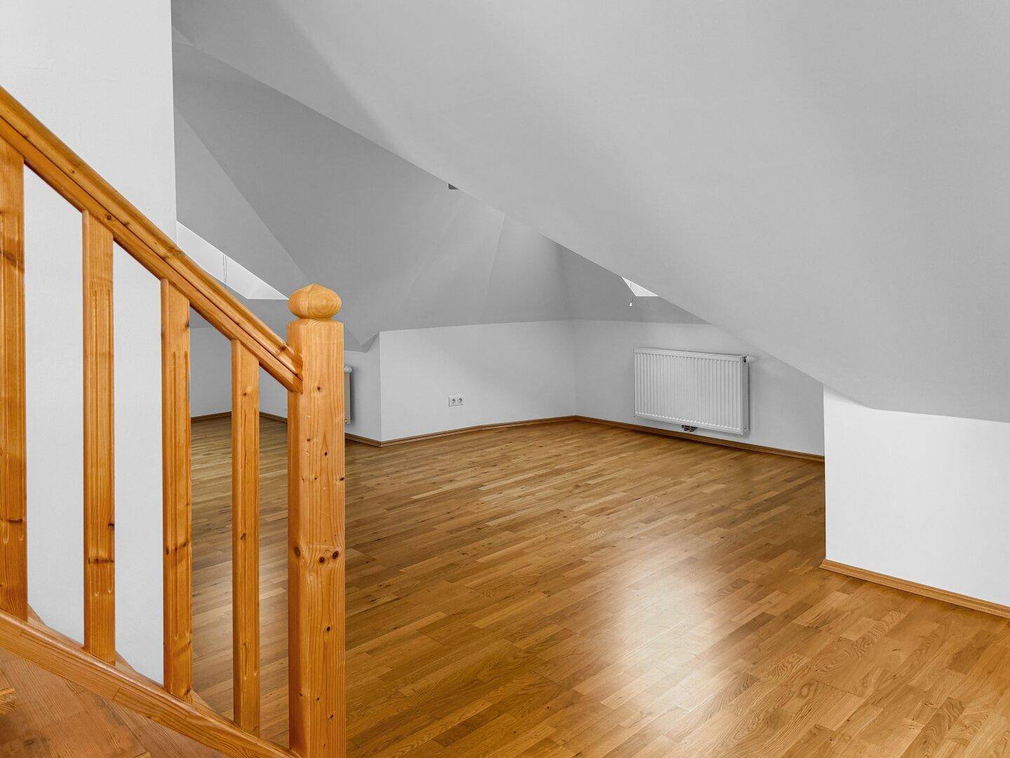 Heller Dachgeschossraum mit Holzboden, Dachschräge und Holztreppe.