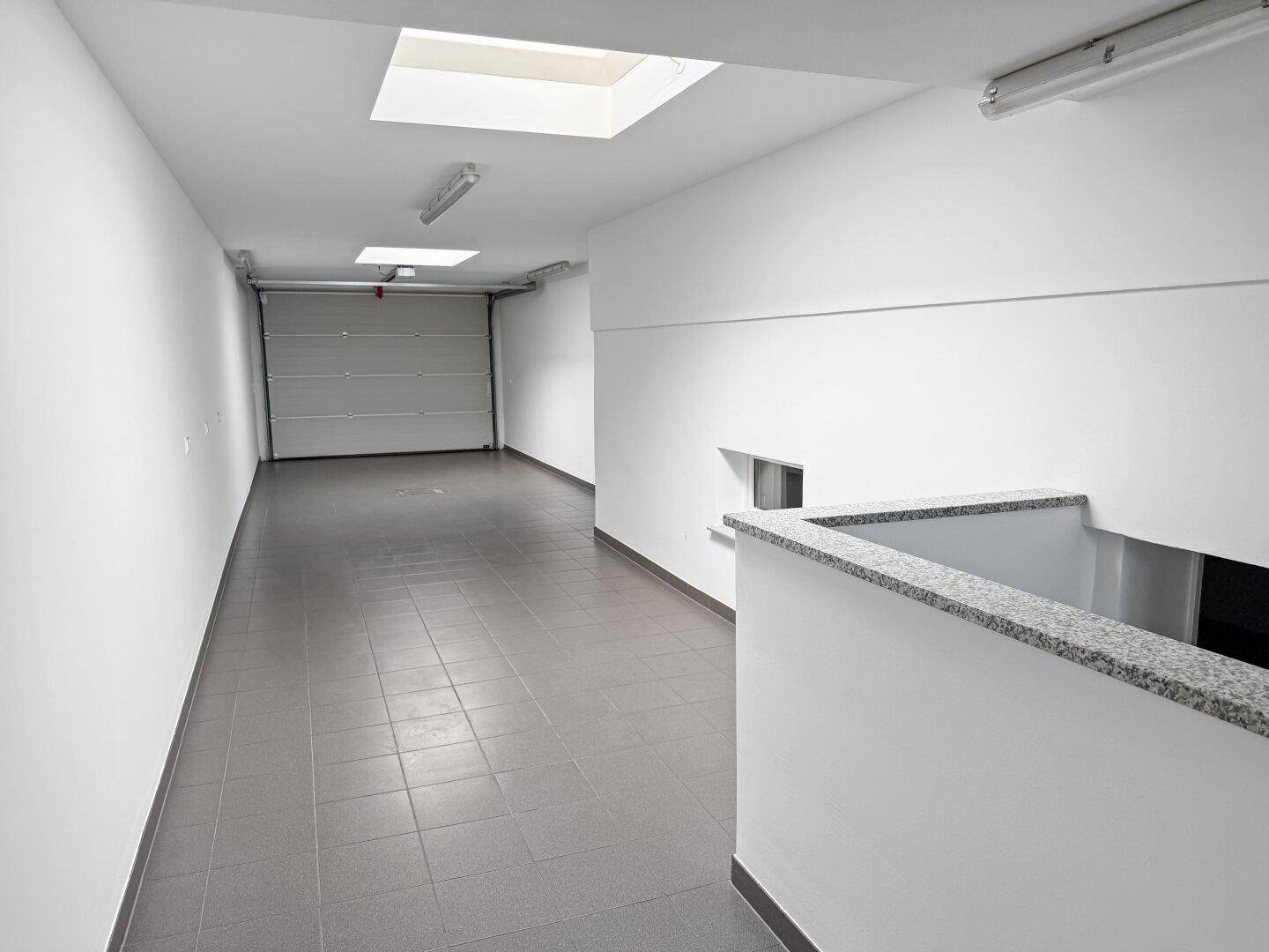 Geräumige Tiefgarage mit Fliesenboden, Rolltor und Oberlichtern.