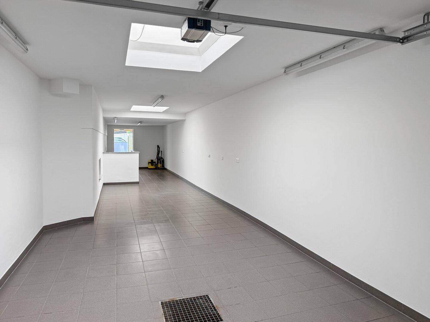 Lange Tiefgarage mit Fliesenboden, Oberlichtern und Zugang zu weiteren Bereichen.