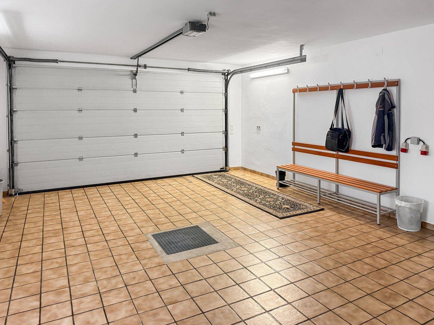 Garage mit Fliesenboden, Rolltor und Garderobe für Arbeitskleidung.