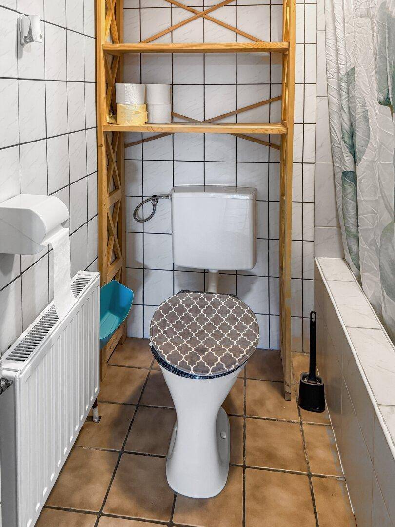 Kleines WC mit Fliesen, Toilette und Holzregal über dem Spülkasten.
