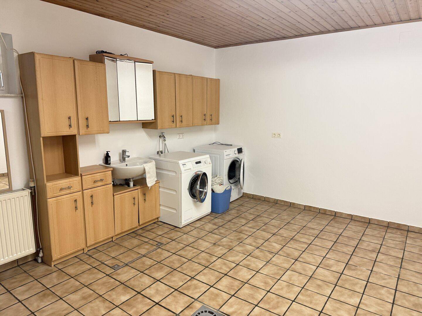 Waschküche mit Waschmaschine, Trockner, Spülbecken und Holzdeckenverkleidung.