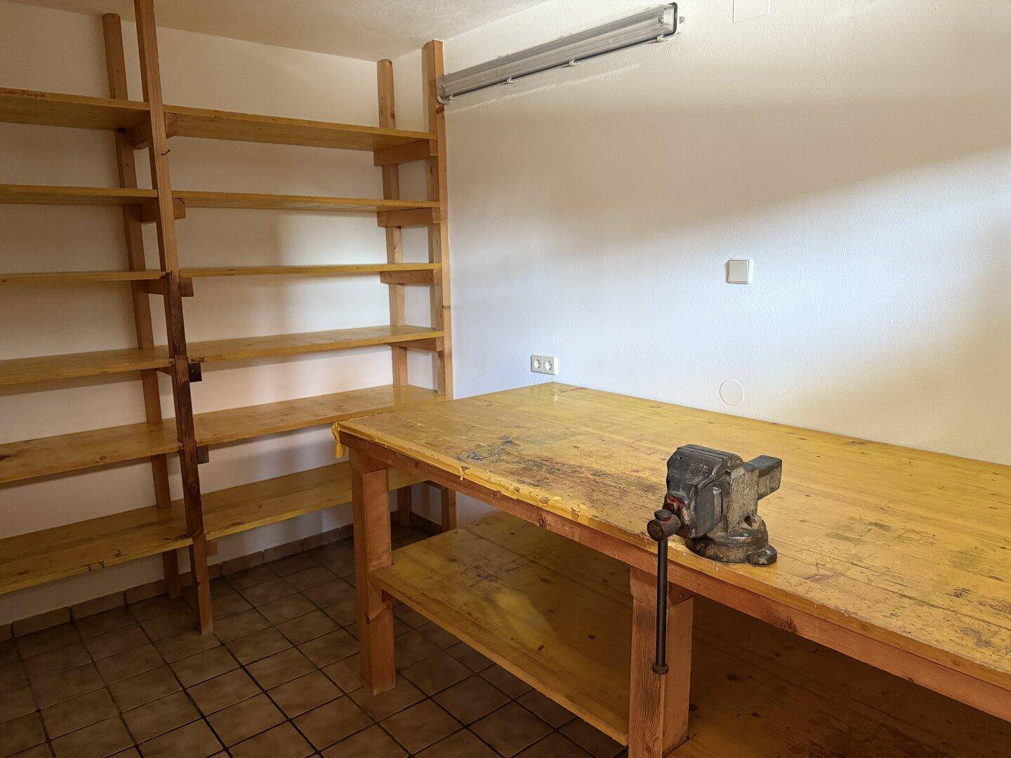 Geräumiger Werkstattraum mit stabilen Holzregalen und einer Werkbank mit Schraubstock.