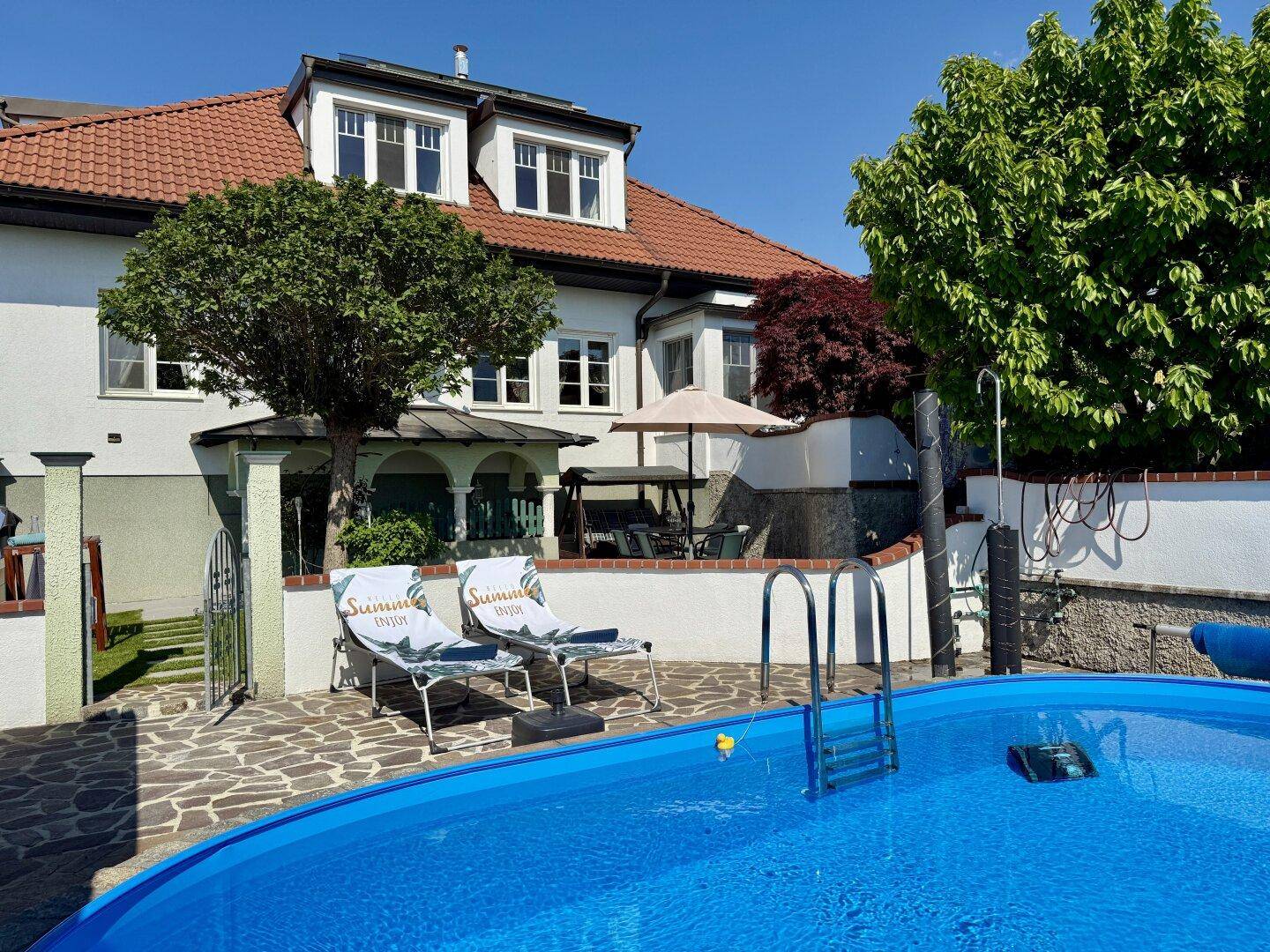 Außenbereich mit Pool, Liegestühlen und gepflasterter Terrasse vor dem Haus.