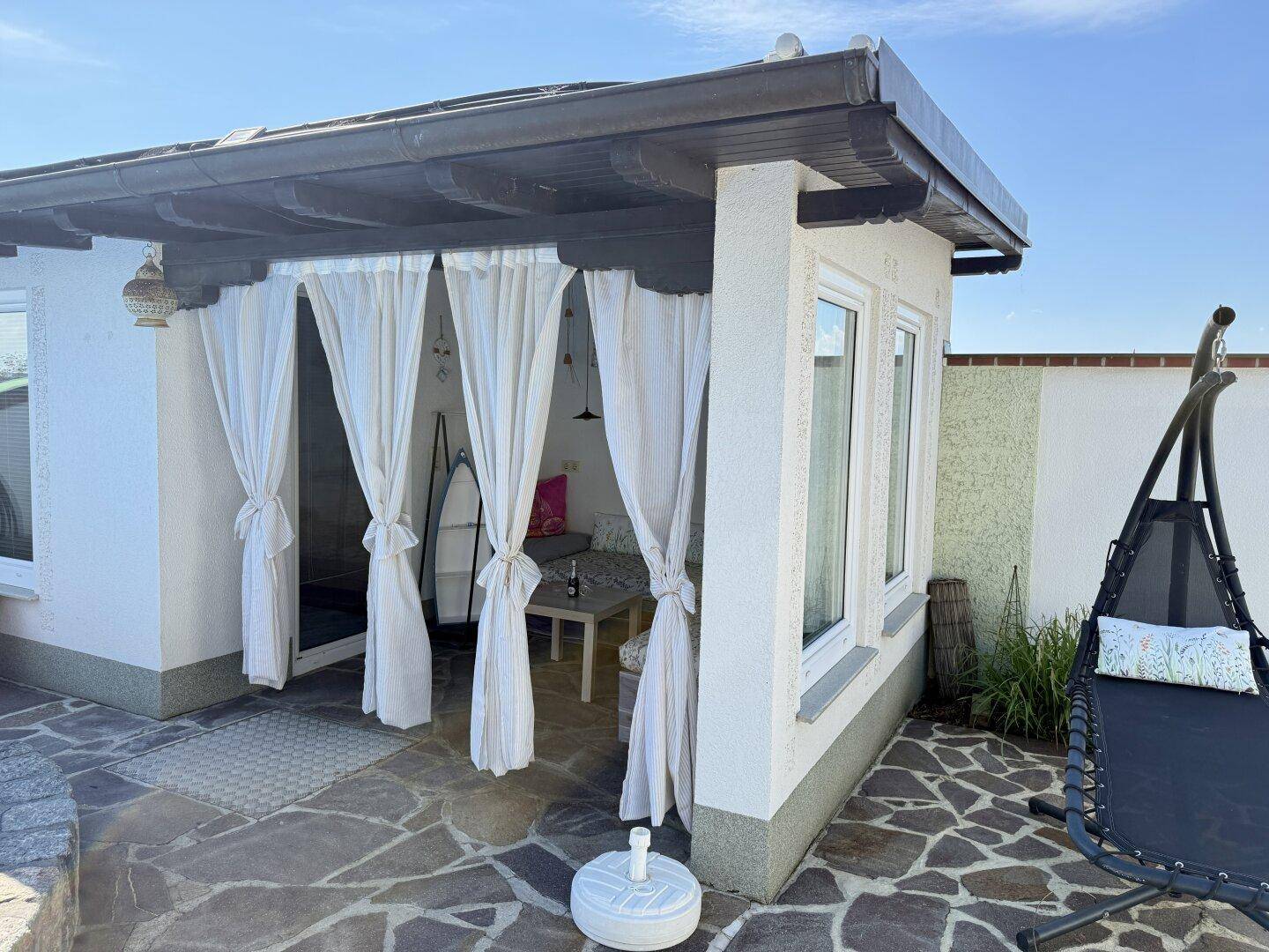 Überdachter Außenbereich mit Vorhängen und Hängesessel, ideal für entspannte Stunden im Freien.
