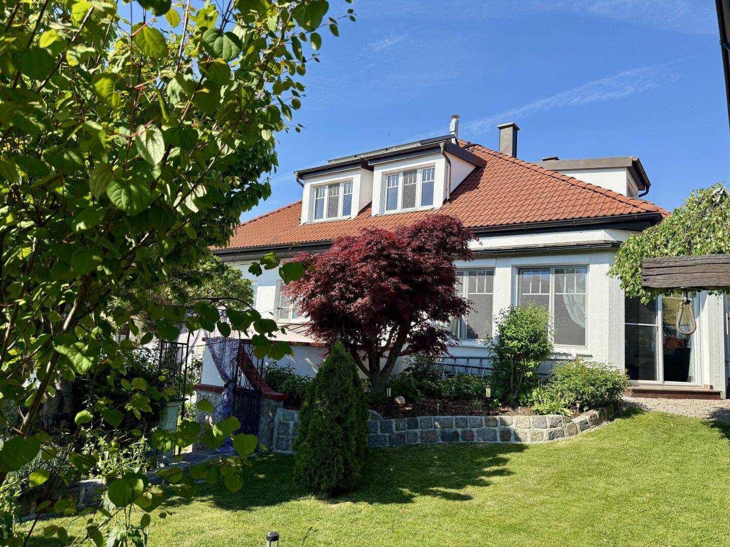 Charmantes Wohnhaus mit rotem Ziegeldach und gepflegtem Garten unter blauem Himmel.