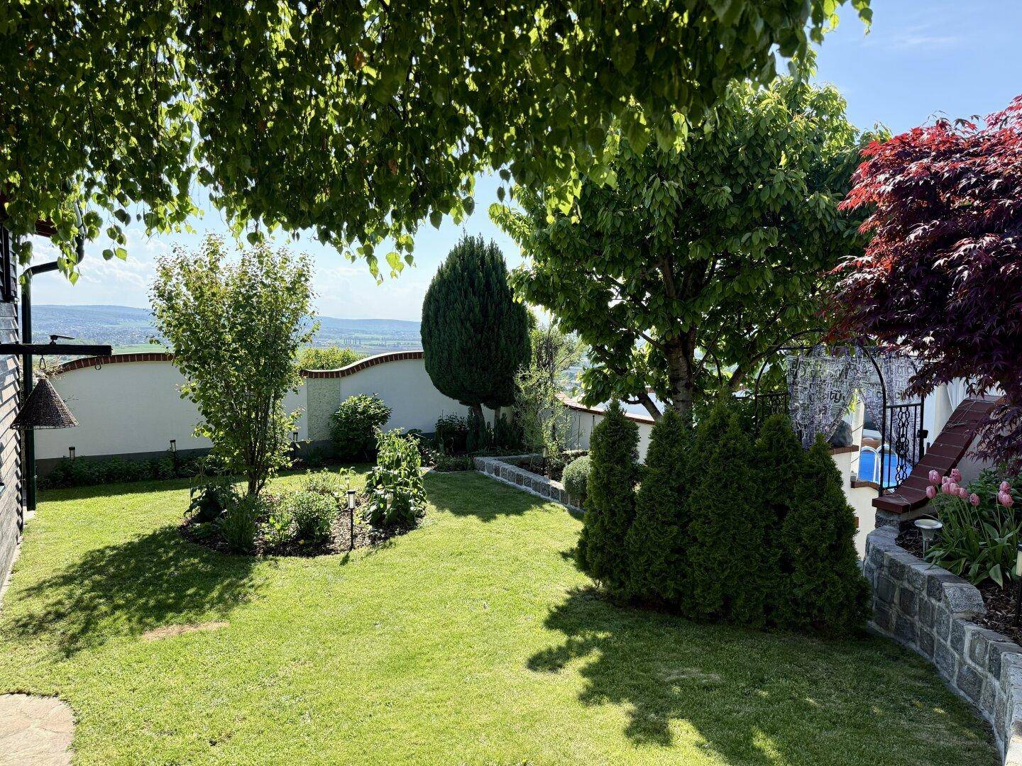 Weitläufiger Rasenbereich im gepflegten Garten mit Bäumen und Fernblick.