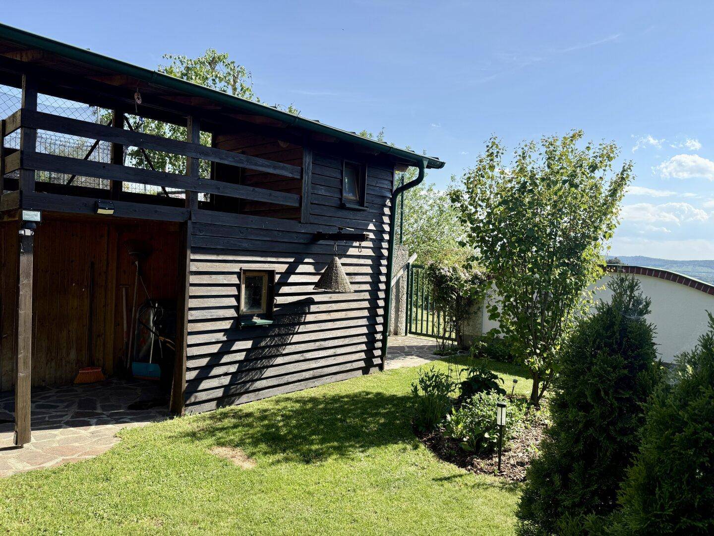 Rustikales Gartenhaus aus Holz mit überdachtem Bereich und angrenzendem Rasen.