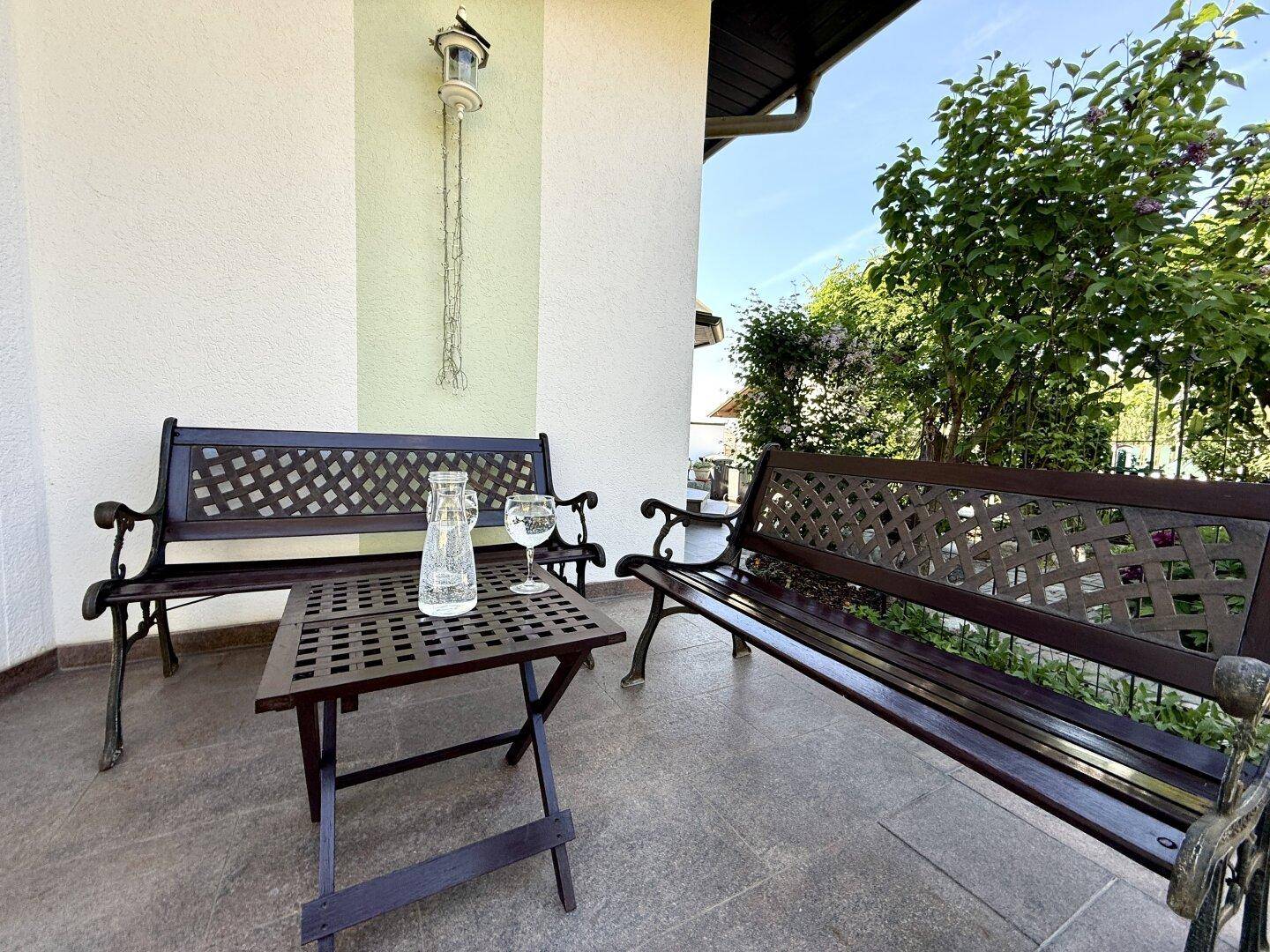 Überdachte Veranda mit zwei Bänken und einem kleinen Tisch, ideal für entspannte Stunden.