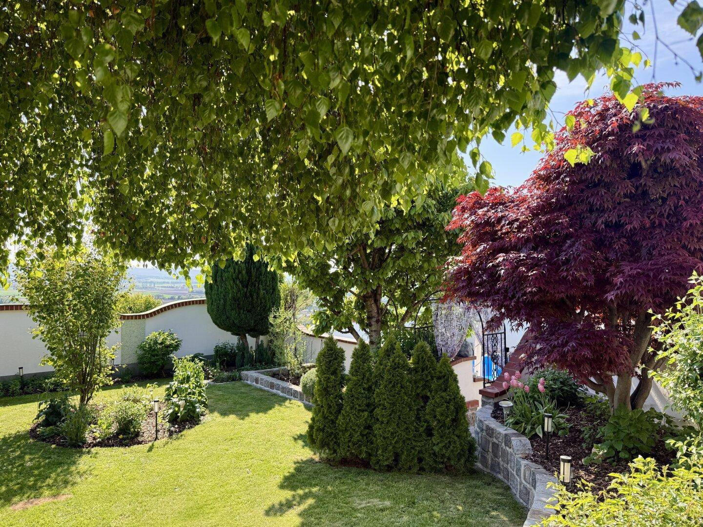 Weitläufiger, gepflegter Garten mit Rasenflächen, Bäumen und Steinbeeten.
