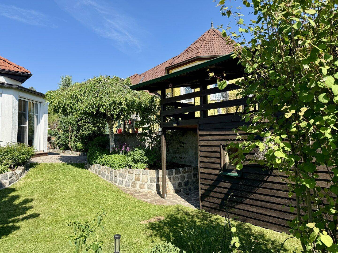 Gepflegter Garten mit Rasen, Bäumen und einem charmanten Holzgebäude im Hintergrund.