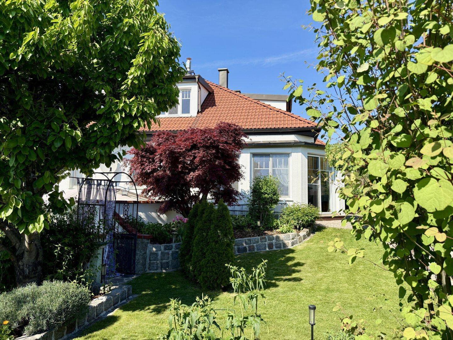 Gepflegter Gartenbereich mit Rasenfläche, Bäumen und Sträuchern vor der Hausfassade.