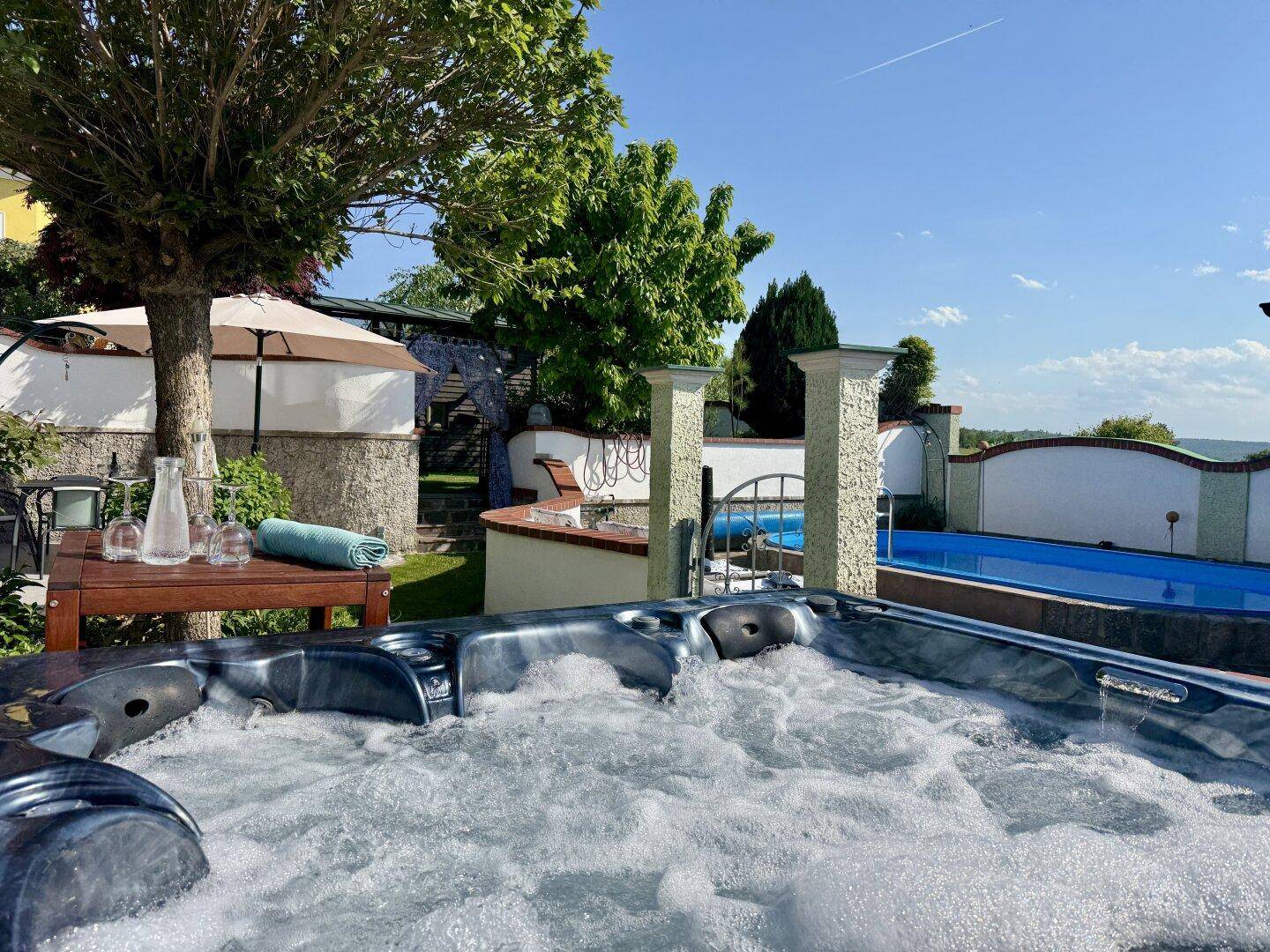 Whirlpool im Garten mit Blick auf den Pool und die weite Landschaft unter blauem Himmel.