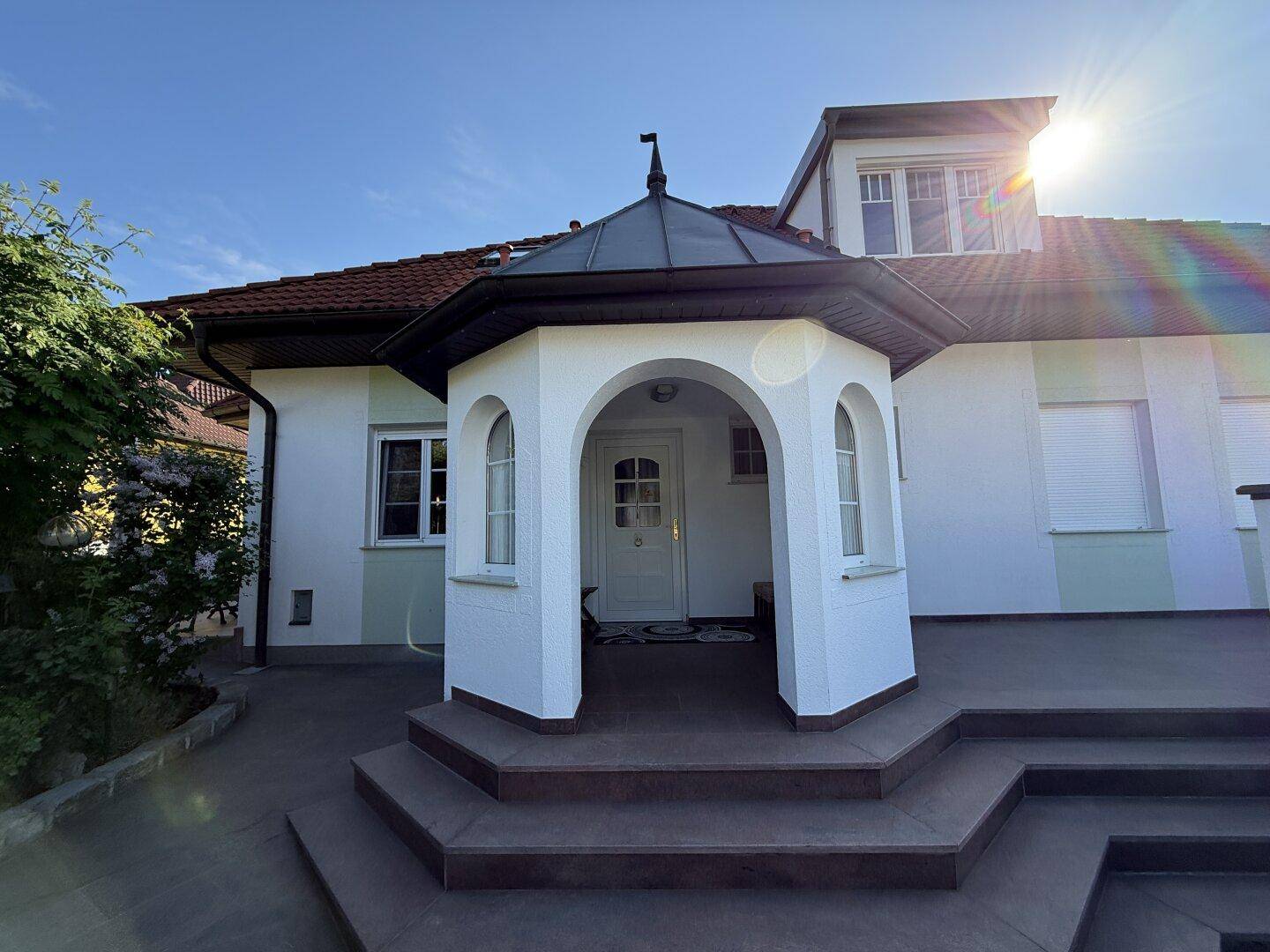 Heller Hauseingang mit architektonischem Erker und sonniger Ausrichtung.