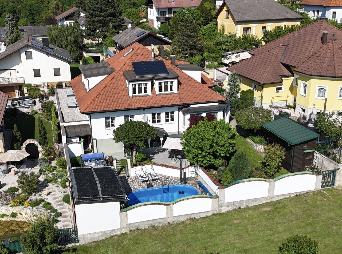 Luftaufnahme eines Hauses mit Pool, Garten und Solaranlagen auf dem Dach in einer Wohnsiedlung.