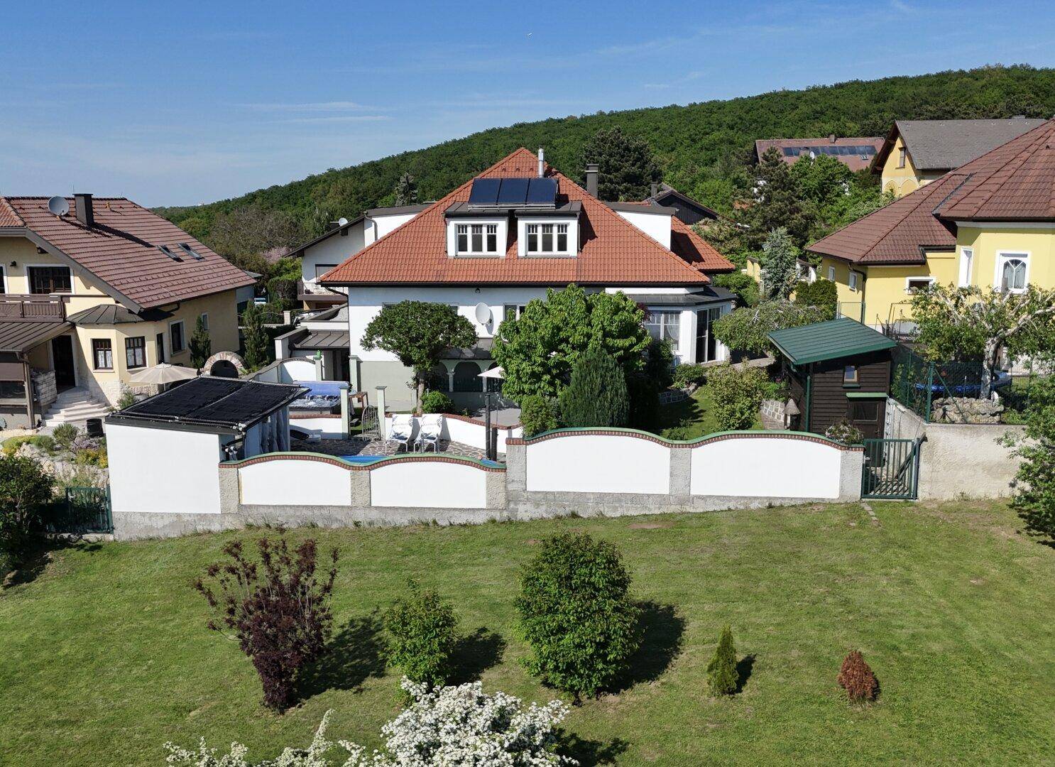 Weitläufige Ansicht des Hauses mit Garten, Poolbereich und umgebender grüner Landschaft unter blauem Himmel.