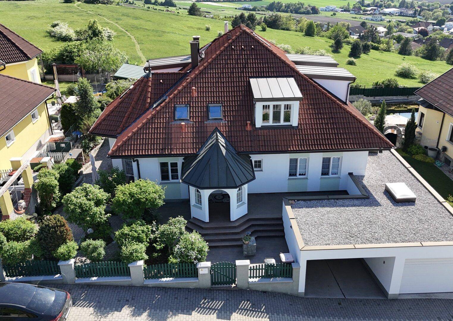 Luftaufnahme eines charmanten Hauses mit rotem Ziegeldach, Garage und gepflegtem Garten.