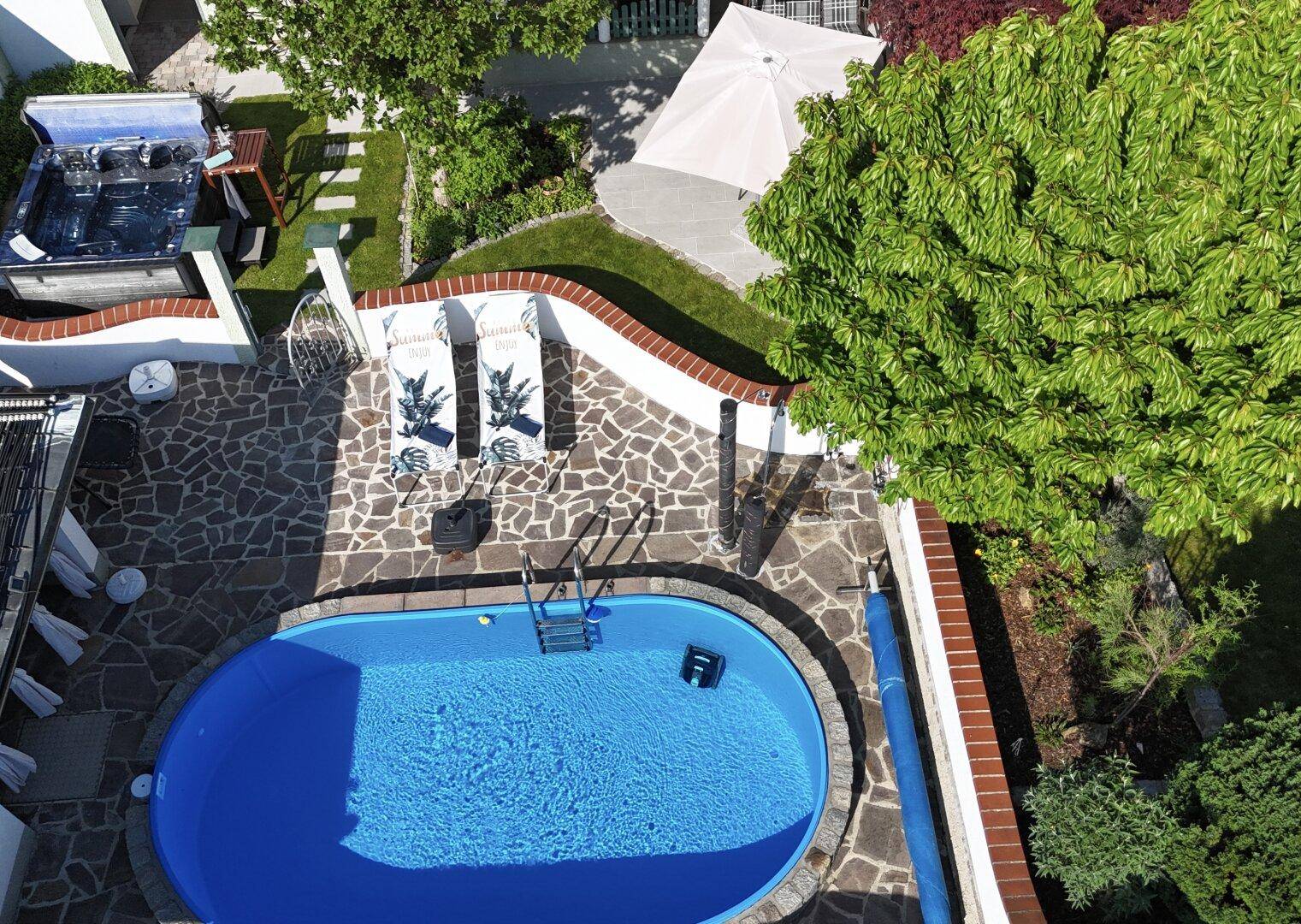 Nahaufnahme des Pools und Whirlpools mit gepflasterter Terrasse und Liegestühlen im Gartenbereich.