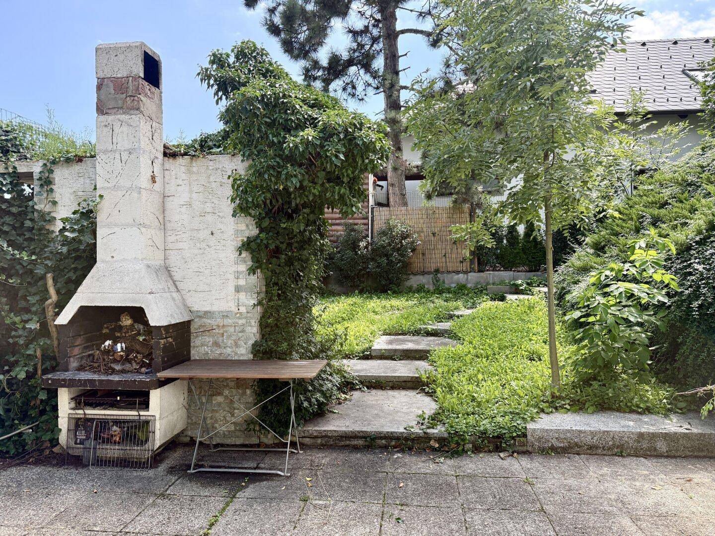 Gemütlicher Grillbereich im Garten mit Steingrill und gepflastertem Boden.