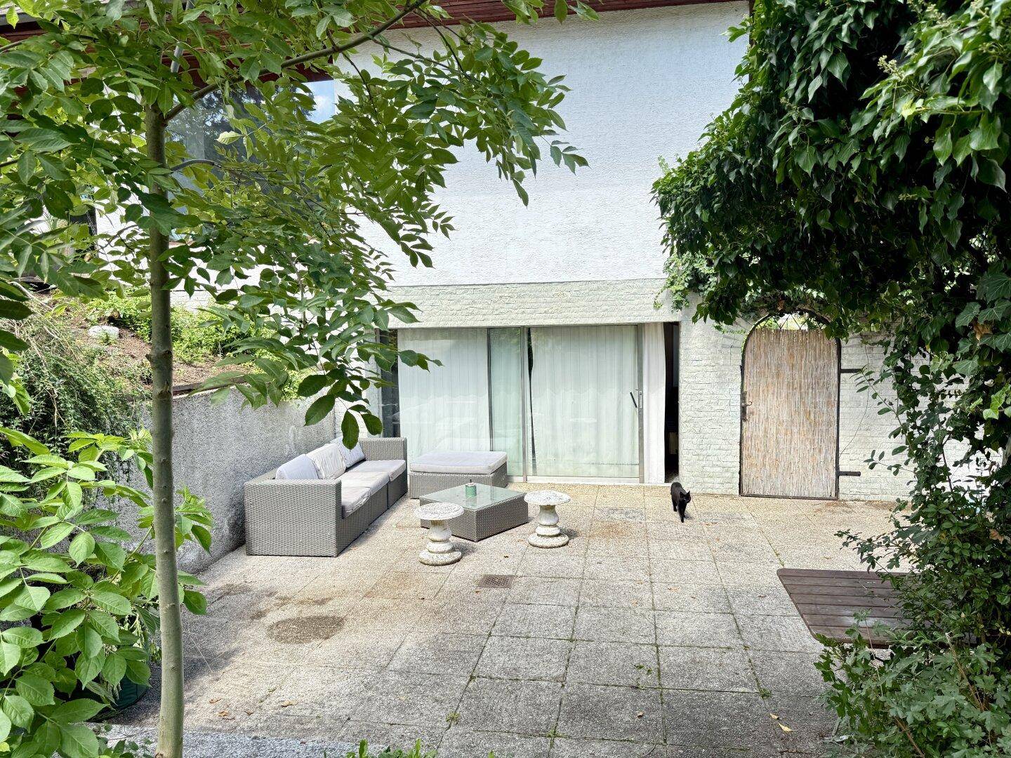 Gepflasterte Terrasse im Garten mit Outdoor-Sofa und direktem Zugang zum Haus.