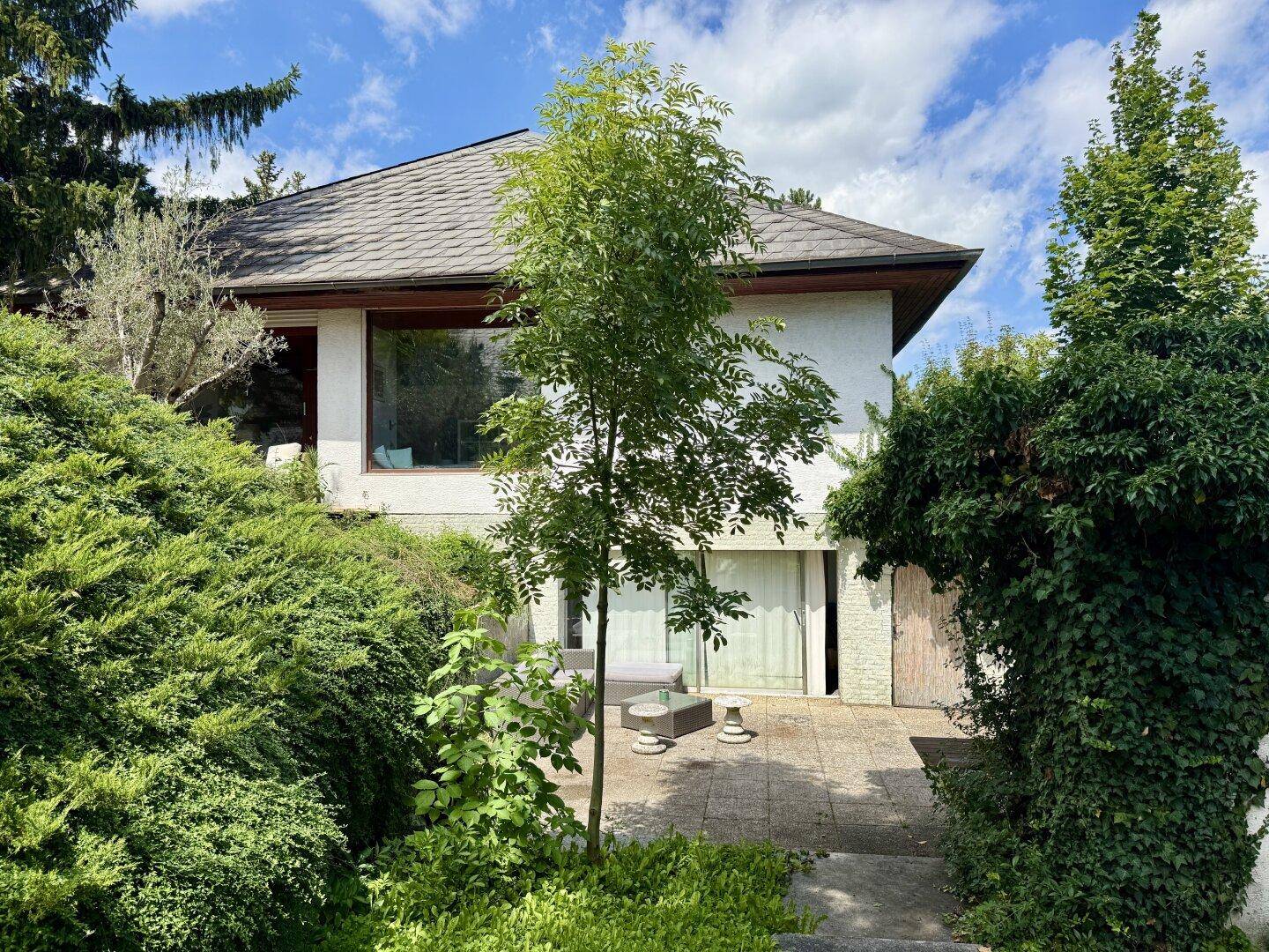 Hausansicht von der Gartenseite mit viel Grün und Terrasse.