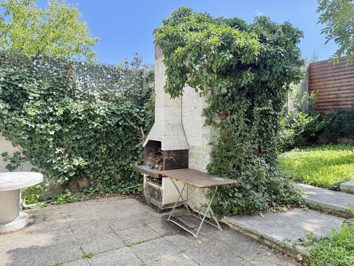 Grillplatz im Garten mit Kamin und üppiger Begrünung.