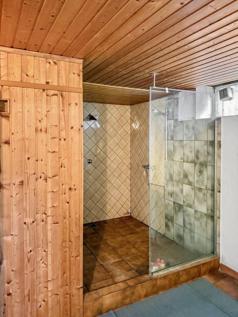 Duschbereich mit Fliesen und Glasabtrennung neben der Sauna.
