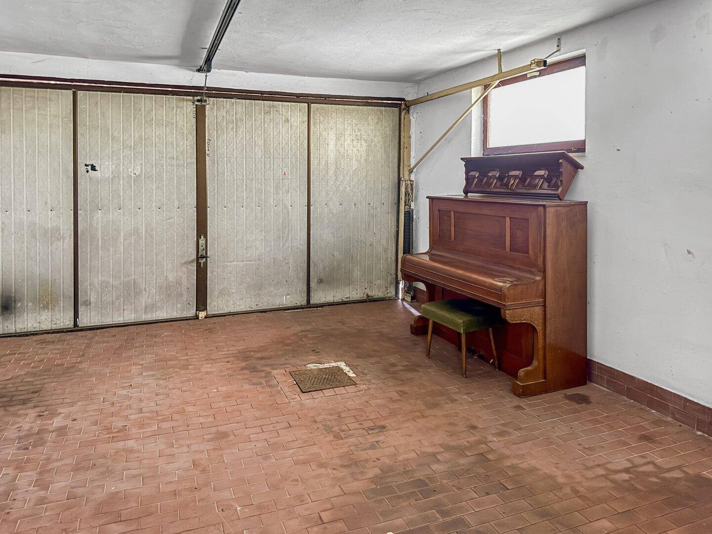Geräumige Garage mit Ziegelboden und einem Klavier.