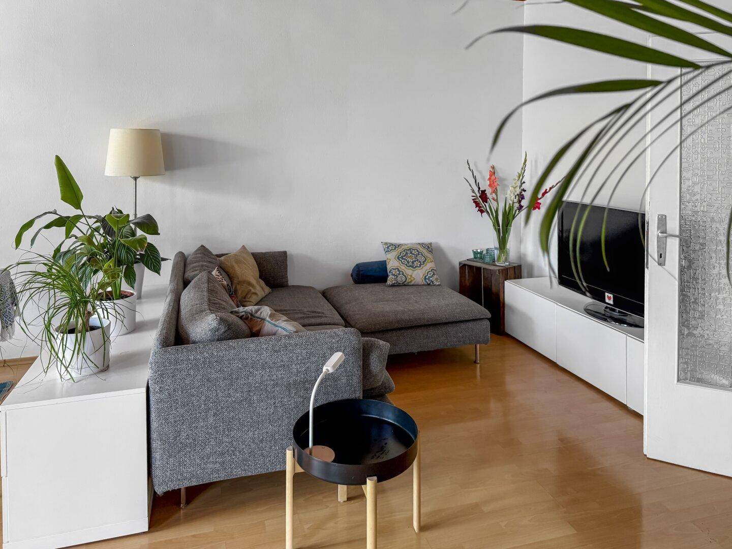 Wohnzimmer mit beigem Sofa, Stehlampe und Blick auf den Fernseher.
