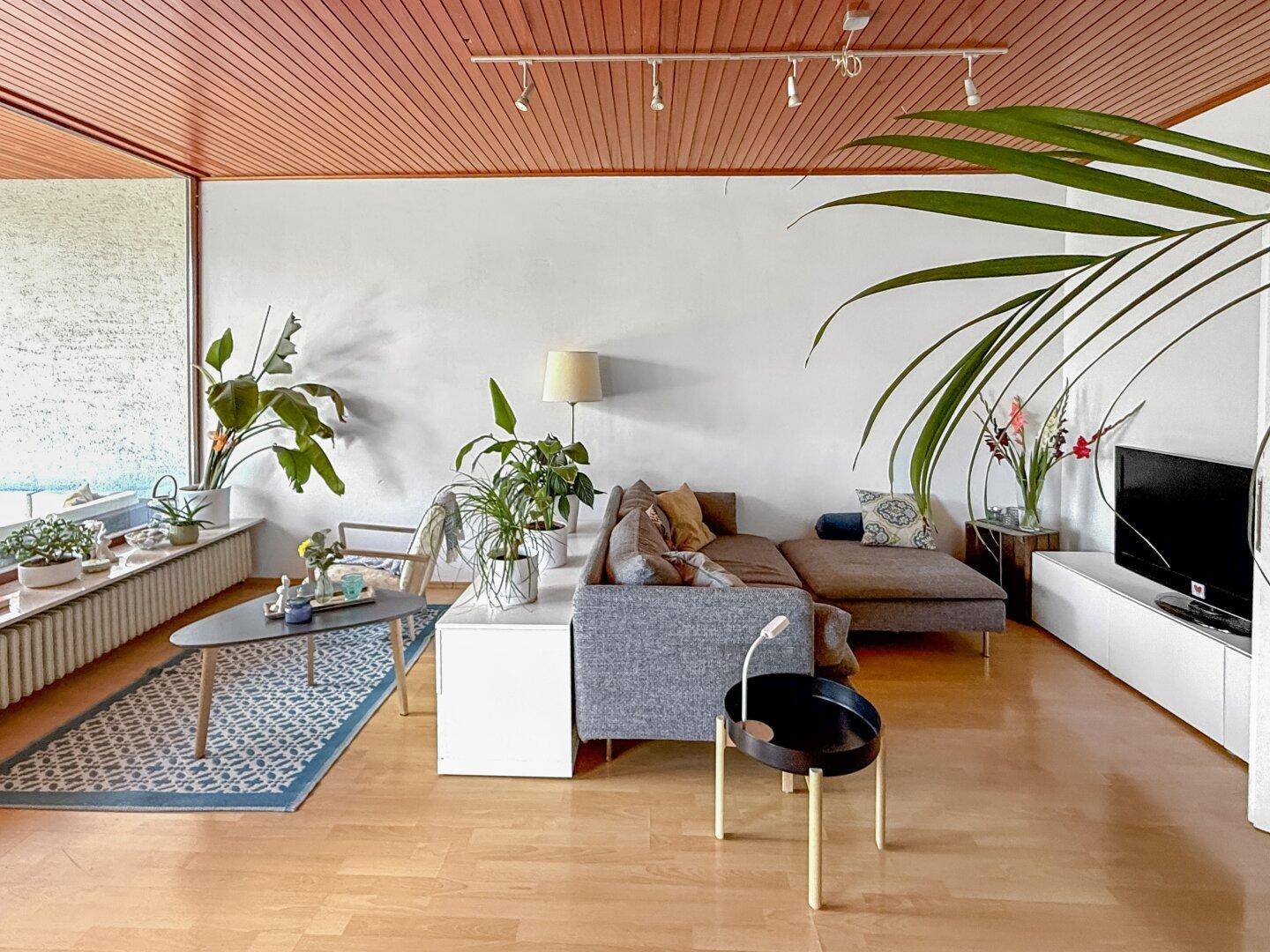 Geräumiges Wohnzimmer mit Holzdecke, Parkettboden und großen Fenstern.