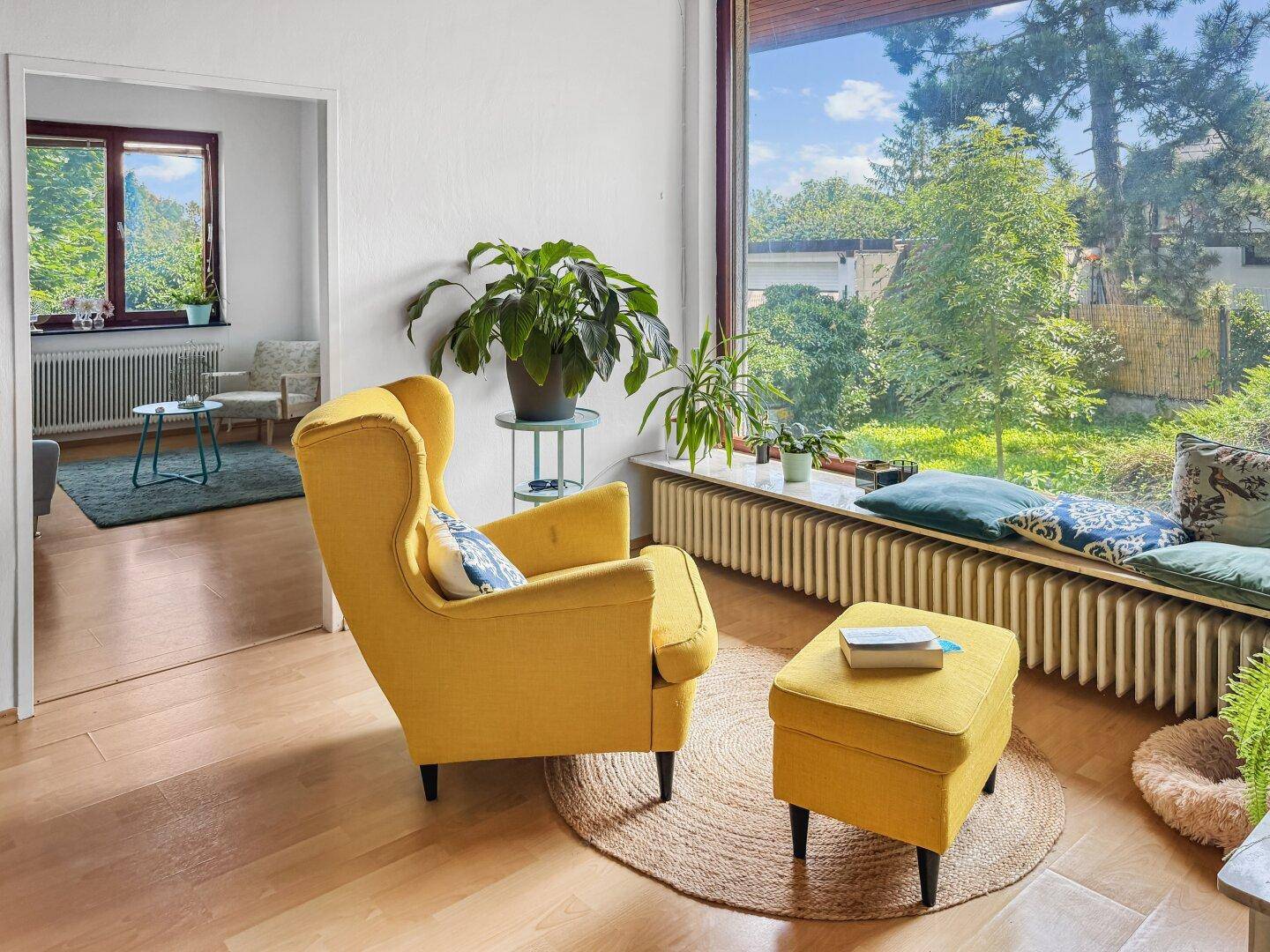 Helles Wohnzimmer mit großem Fenster, gelbem Sessel und Parkettboden.
