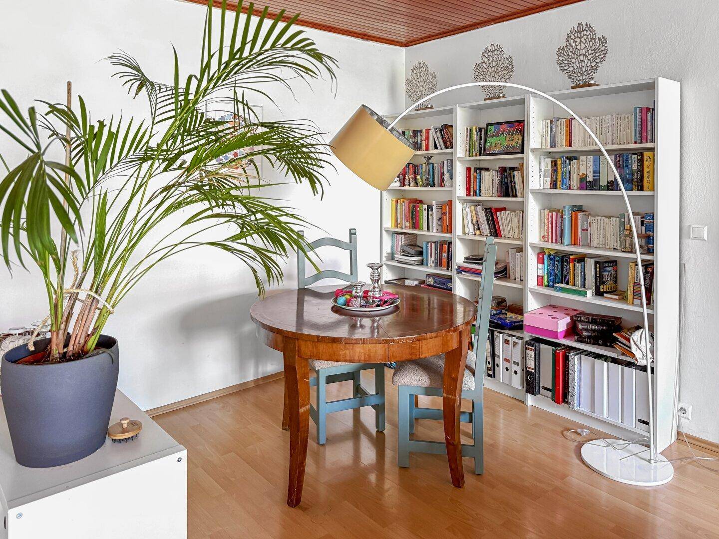 Essbereich mit rundem Holztisch, Stühlen und Bücherregalen an der Wand.
