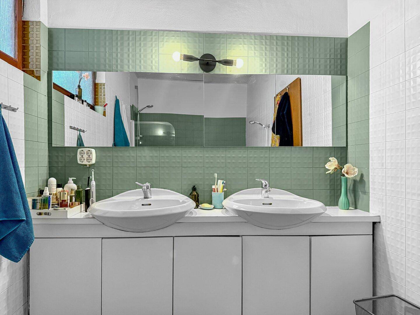 Modernes Badezimmer mit Doppelwaschbecken, großem Spiegel und grünen Fliesen.