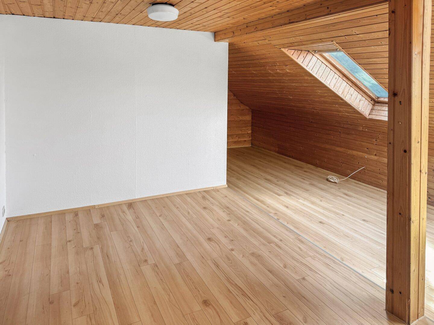 Helles Dachzimmer mit Holzverkleidung, Holzboden und Dachfenster.