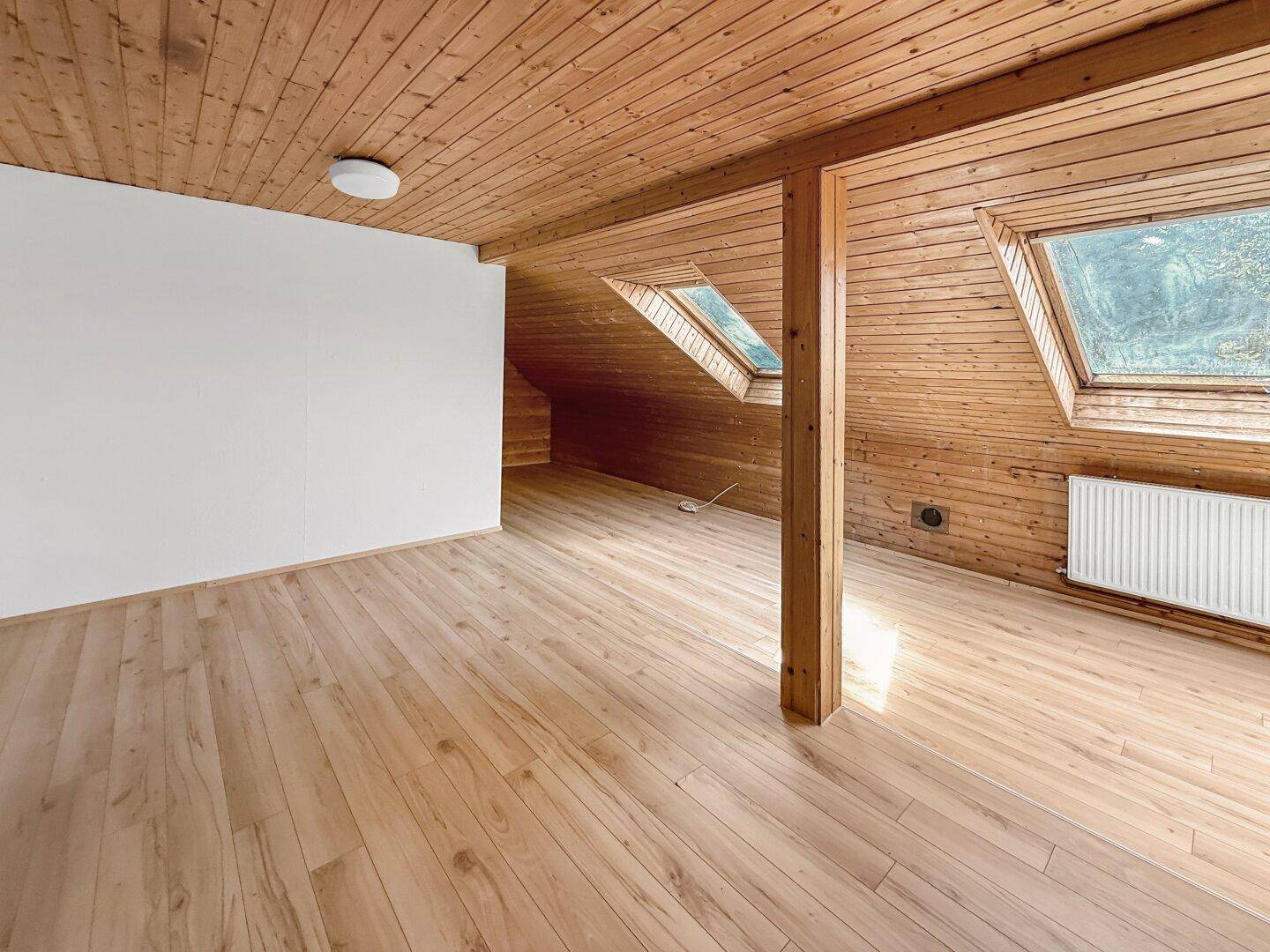 Geräumiges Dachzimmer mit Holzdecke, Holzboden und zwei Dachfenstern.