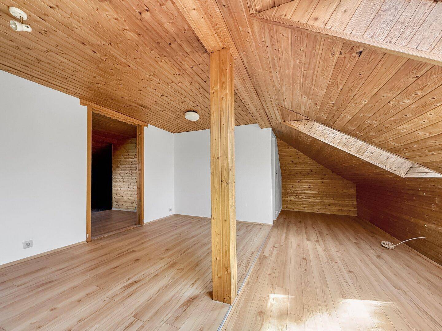 Dachzimmer mit Holzverkleidung, Holzboden und offenem Durchgang zu einem weiteren Bereich.