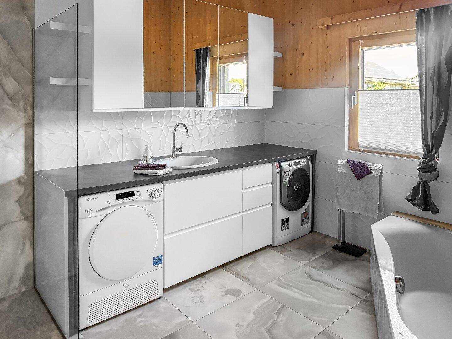 Modernes Badezimmer mit Waschmaschine, Trockner, Badewanne und stilvollen Fliesen.