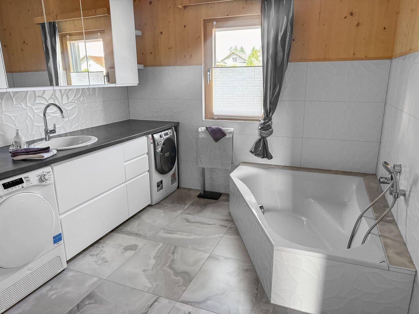 Helles Badezimmer mit Badewanne, Waschtisch, Waschmaschine und Trockner.