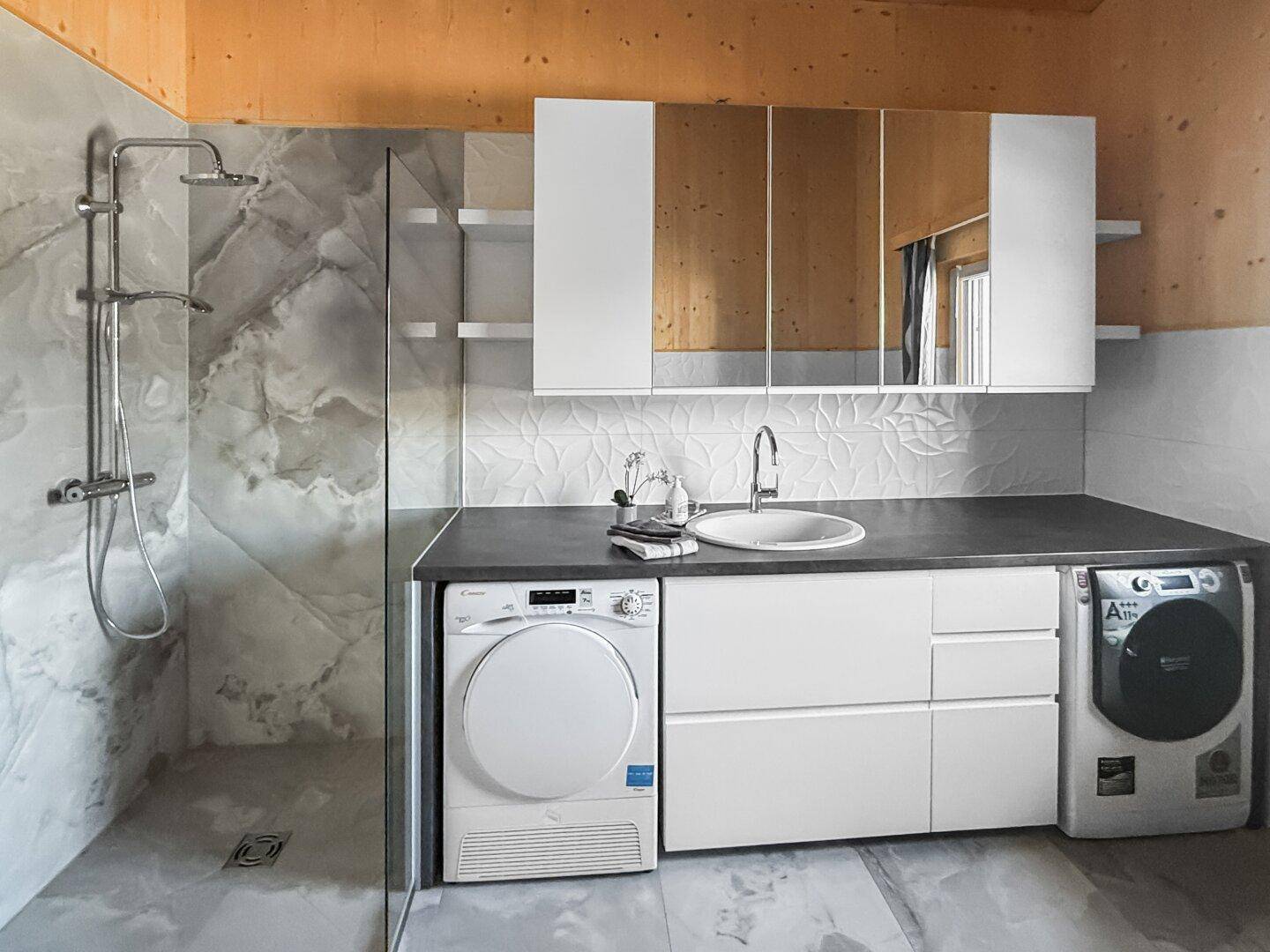 Geräumiges Badezimmer mit begehbarer Dusche, Waschtisch, Waschmaschine und Trockner.