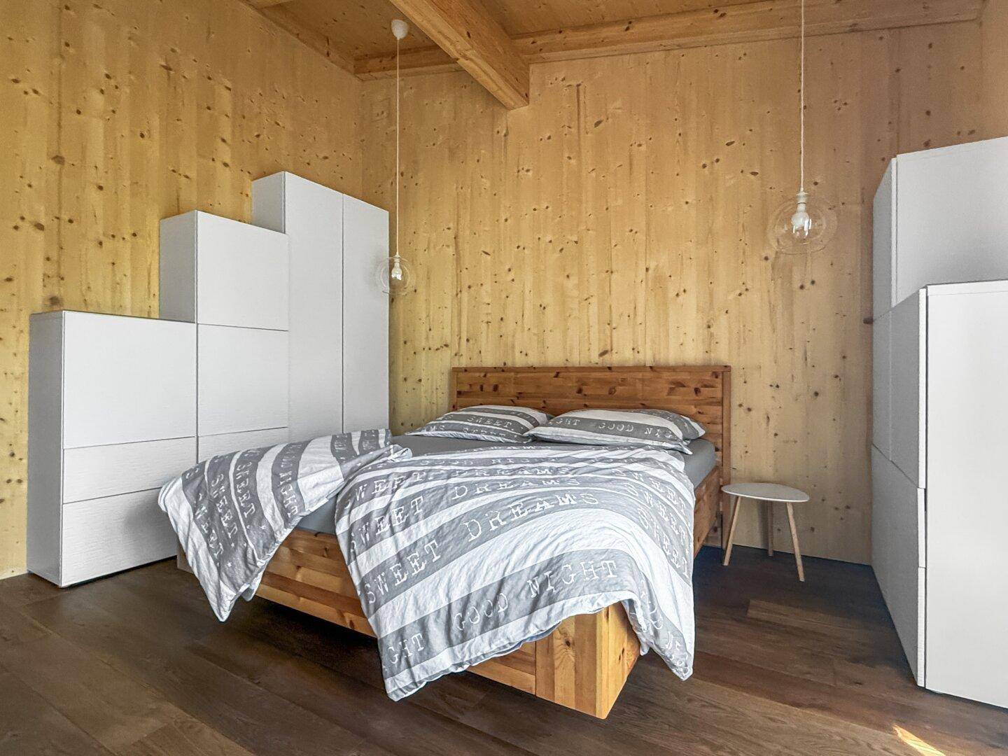 Geräumiges Schlafzimmer mit Holzwänden, Holzboden und modernen weißen Schränken, die viel Stauraum bieten.