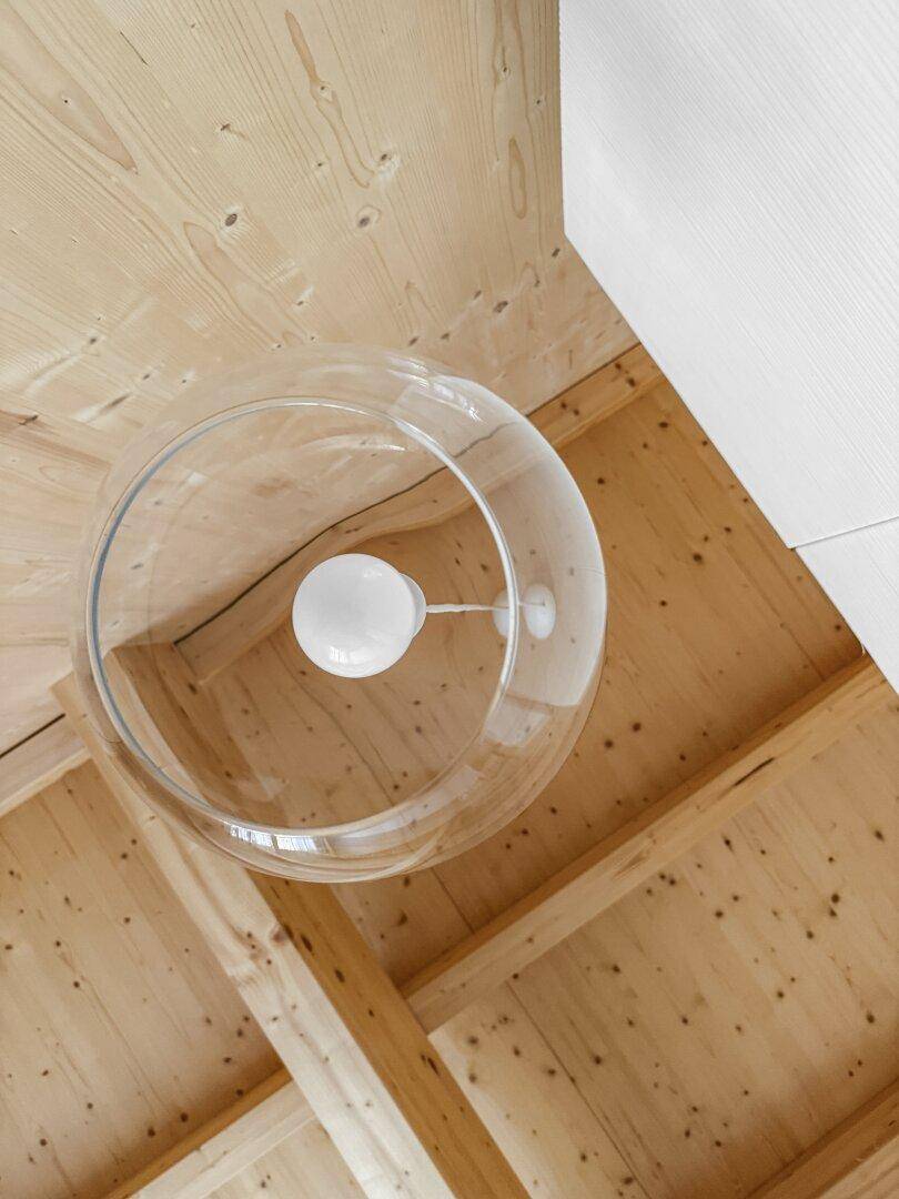 Detailaufnahme der Holzbalkendecke mit moderner Glaspendelleuchte, die den Raum erhellt.
