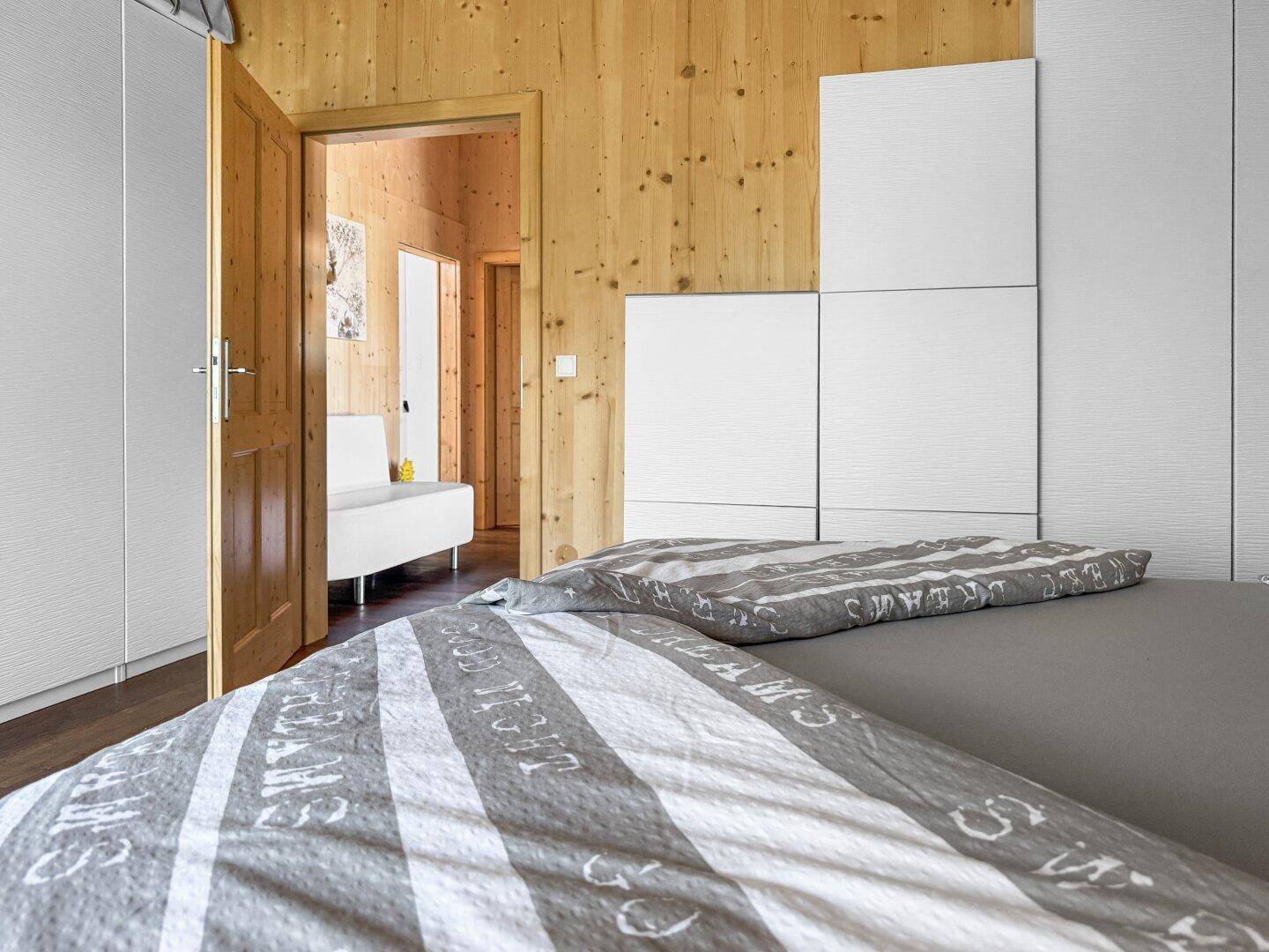 Schlafzimmer mit Holzwänden und dunklem Holzboden, verbunden mit dem Flur durch eine Holztür.