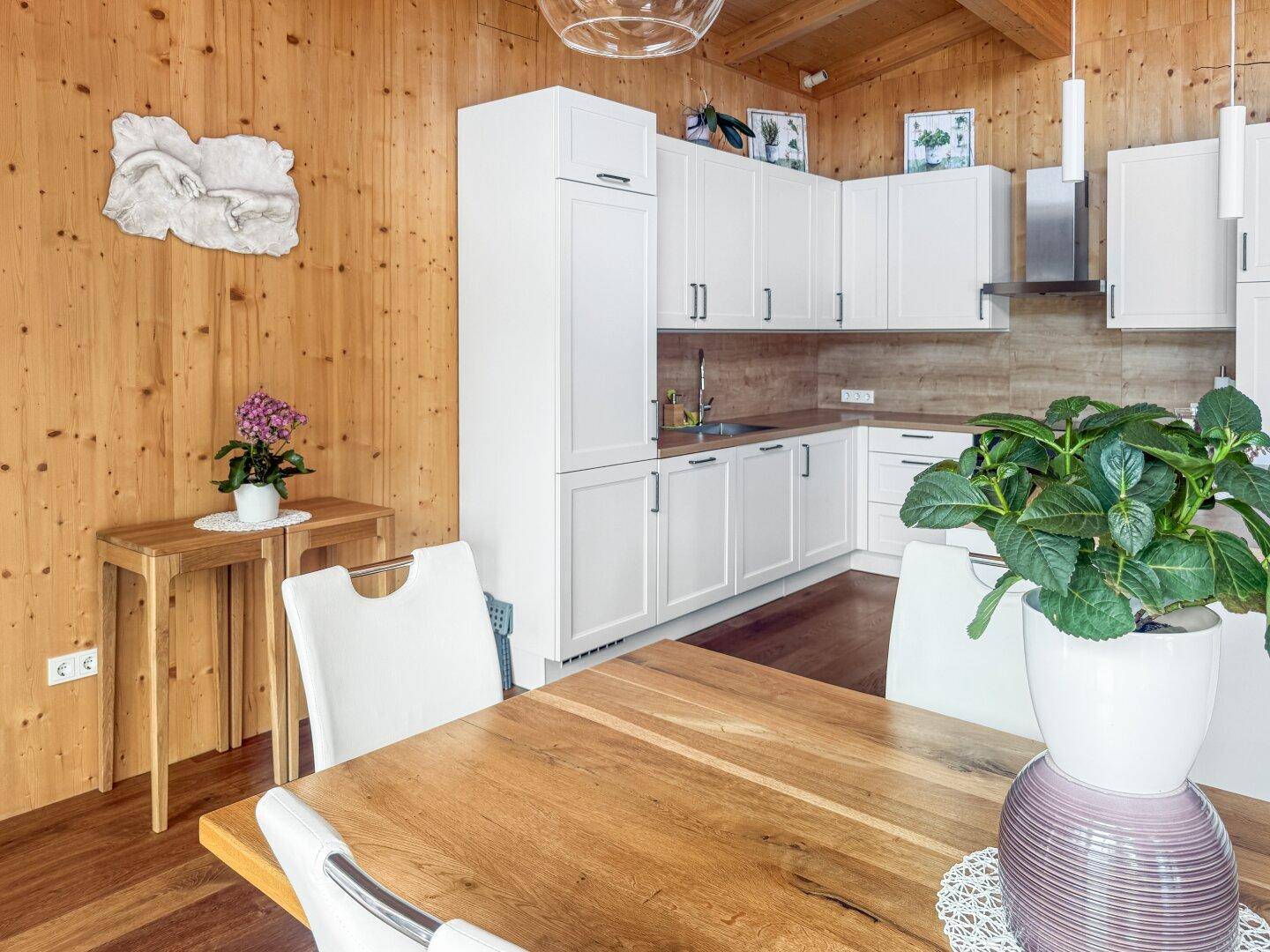 Essbereich mit Holztisch und Blick auf die moderne Küche, umgeben von Holzwänden und warmem Licht.