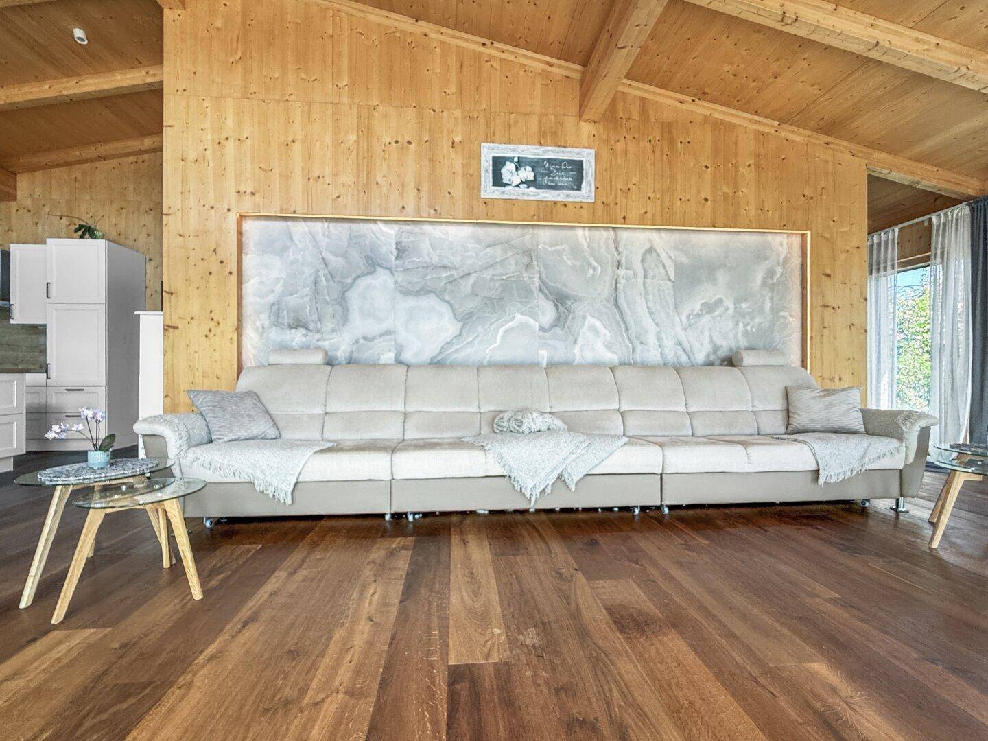 Großzügiges Wohnzimmer mit langem Sofa, Holzwänden und einer eleganten Wanddekoration.