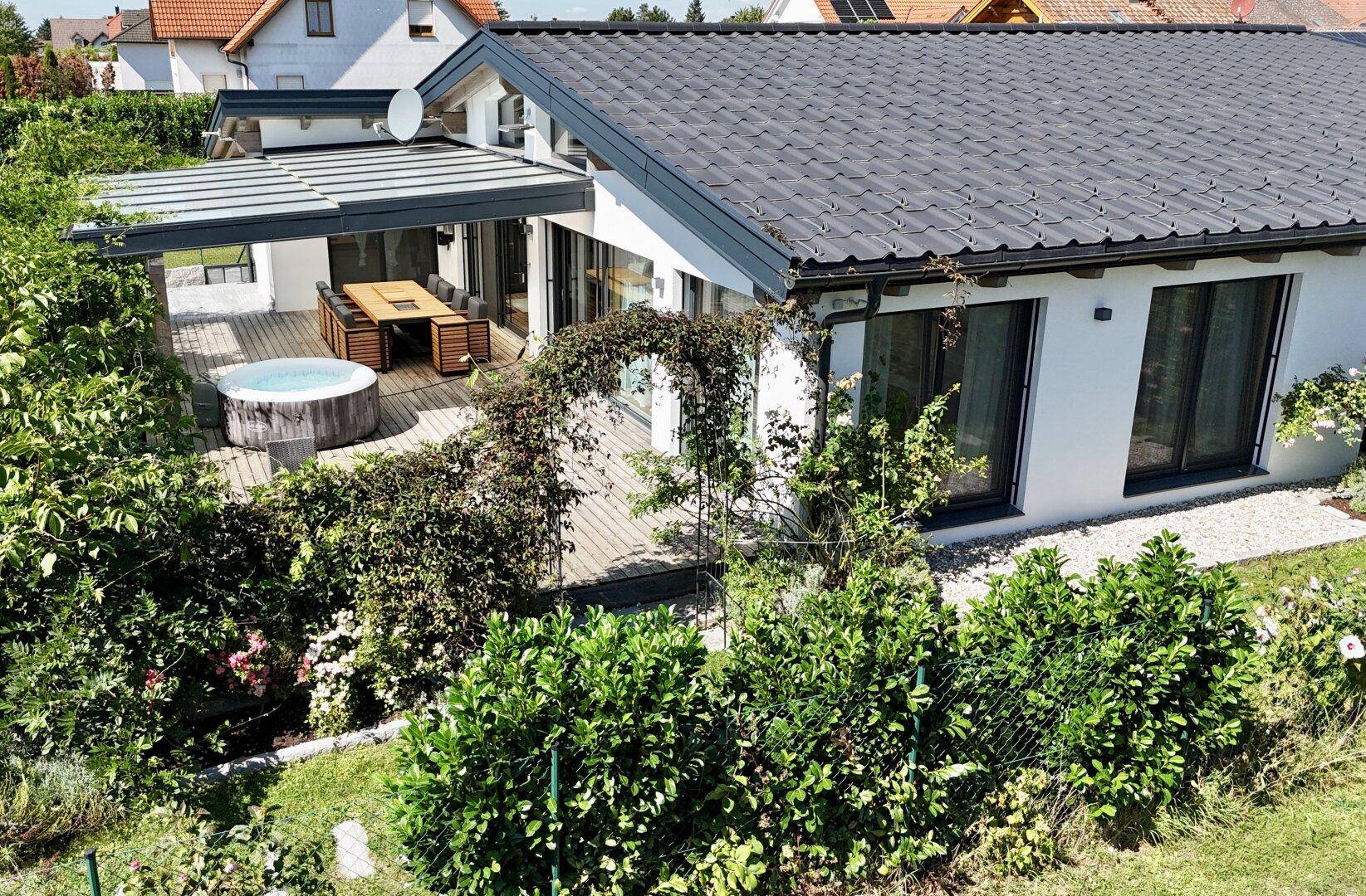Hinteransicht des Hauses mit großer Holzterrasse, Whirlpool und überdachtem Essbereich.